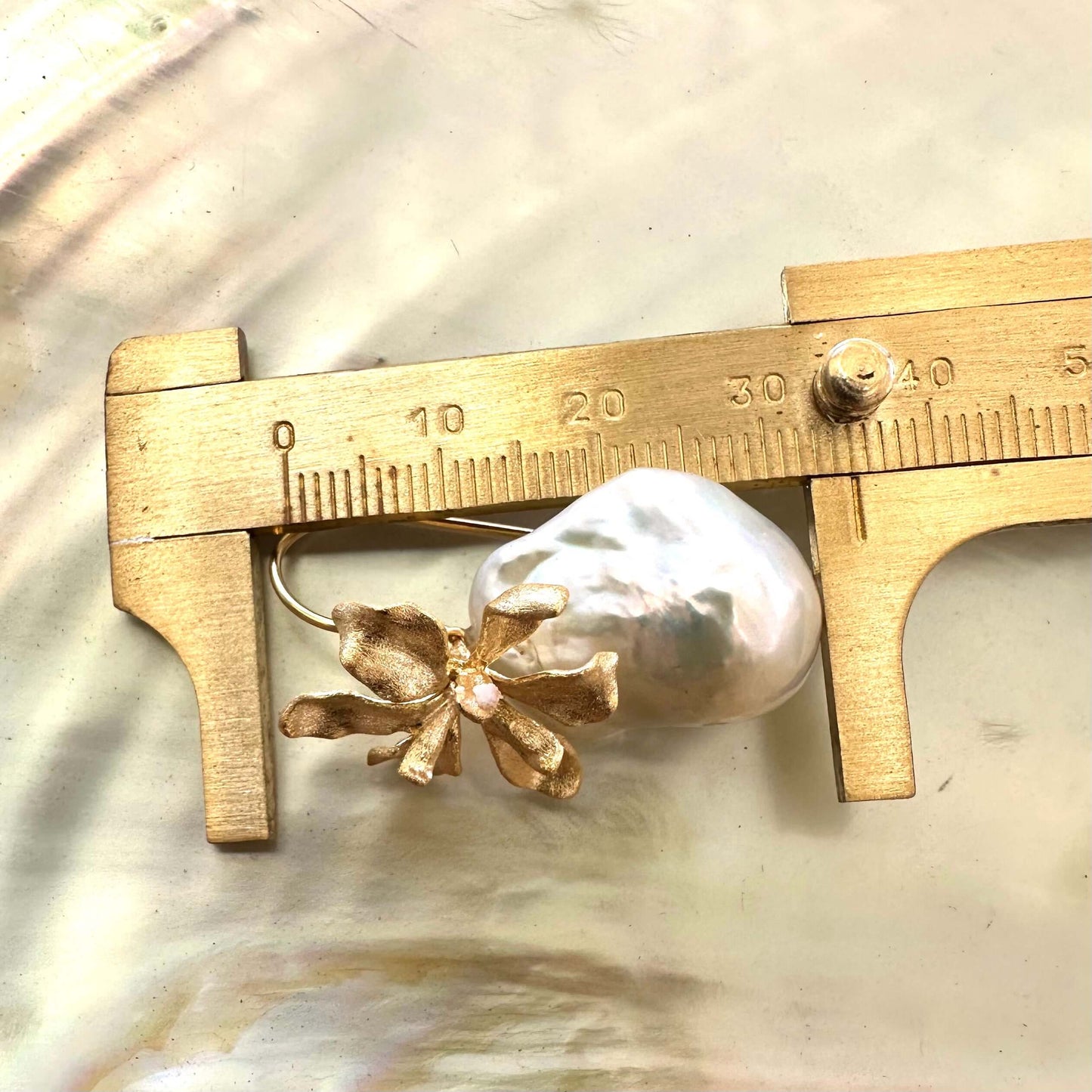 Close-up of gold baroque pearl drop earrings measured with ruler for size