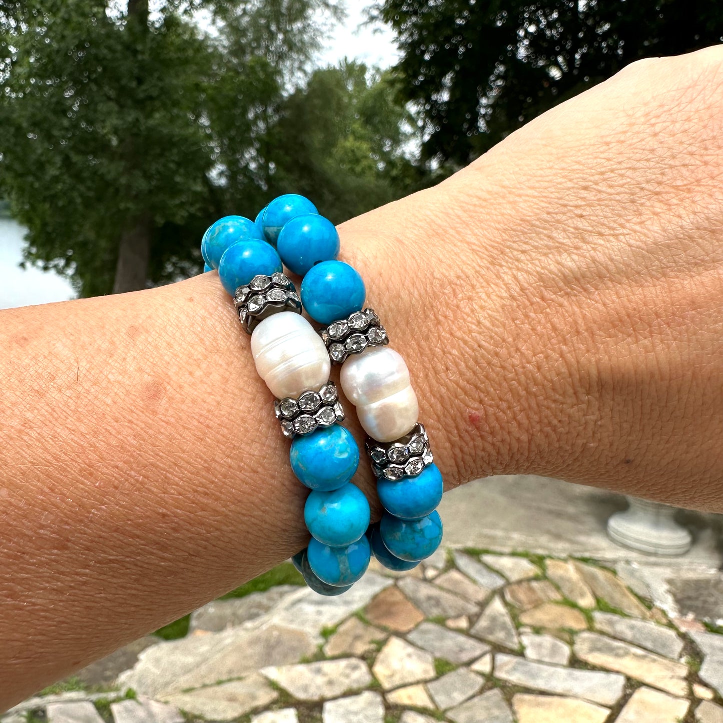 Two turquoise howlite pearl bracelets stacked on wrist near water in garden