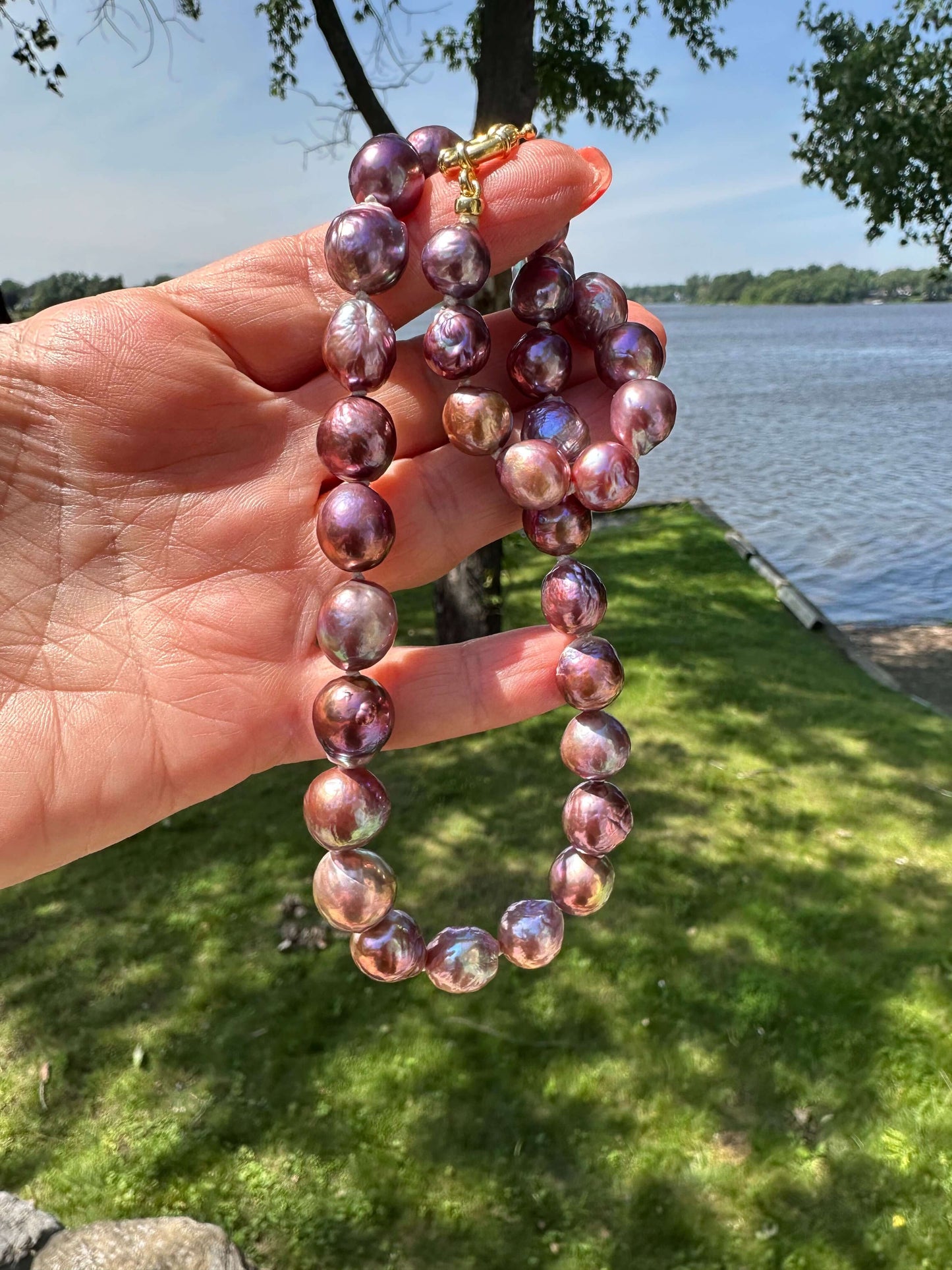 Purple Edison baroque pearl necklace shown in hand with foliage background