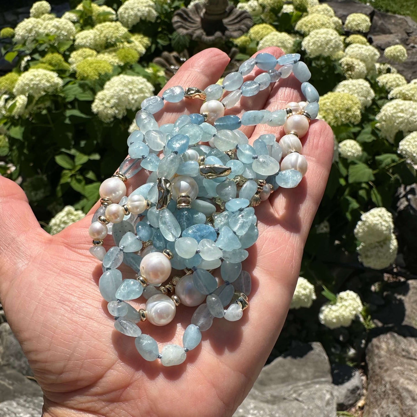 Close-up of aquamarine and pearl necklace held outdoors near green leaves