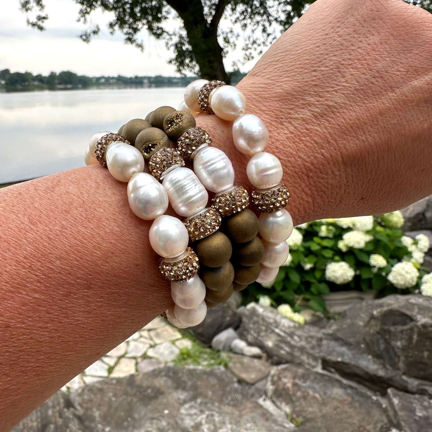 White pearl stretch bracelet set worn on wrist surrounded by green foliage