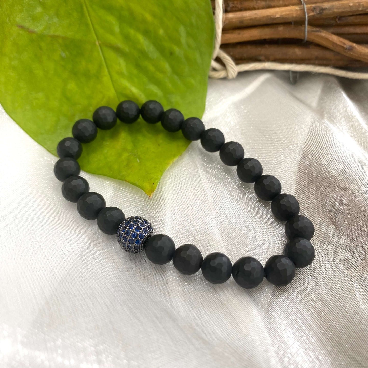 Matte black onyx mens bracelet showcasing 8mm faceted beads and a blue CZ center charm.
