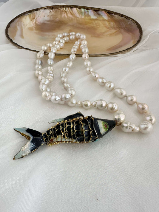 Fish pendant pearl necklace featuring a black cloisonné fish and white baroque pearls in a stylish arrangement.