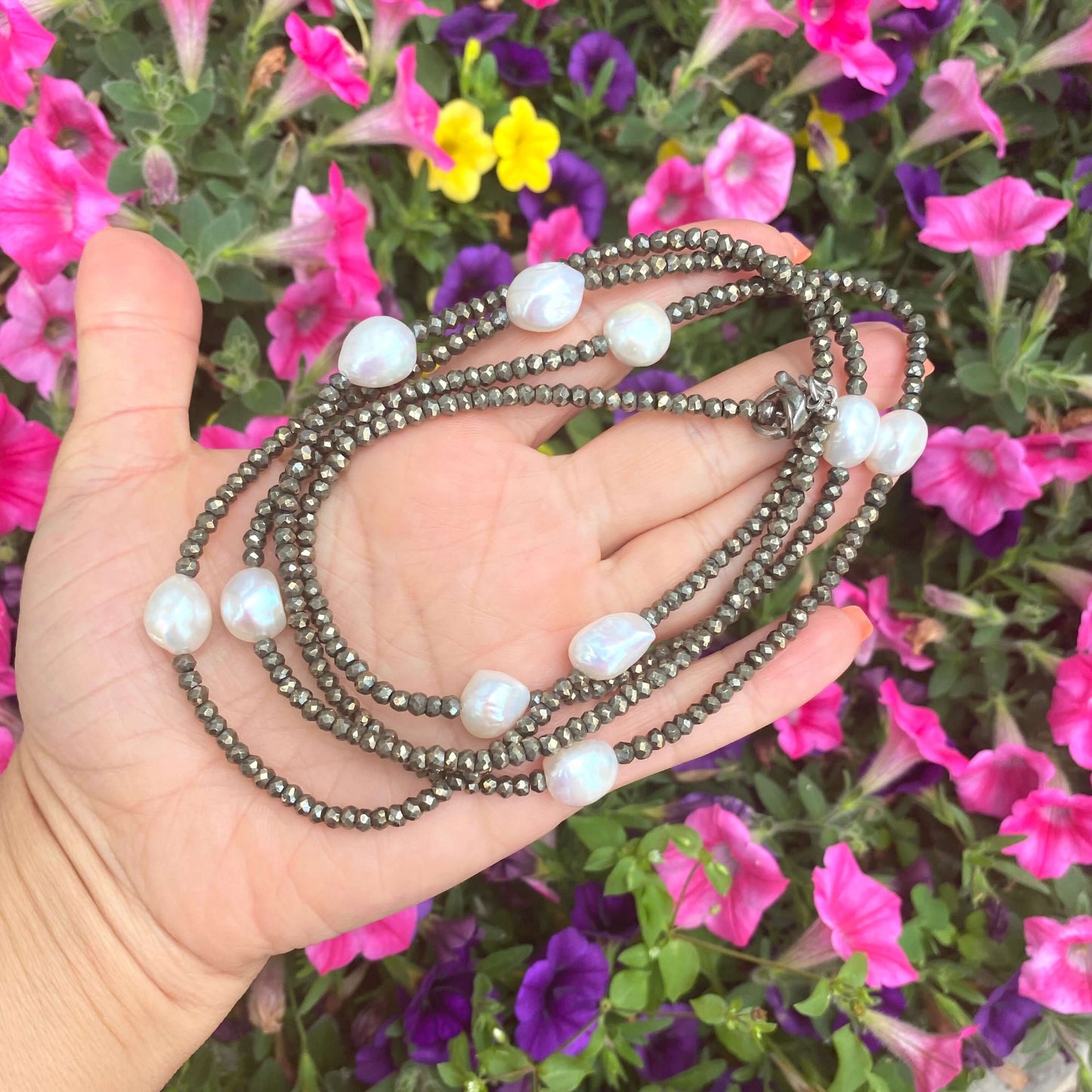 Pyrite pearl long necklace displayed in hand, featuring faceted pyrite beads and freshwater pearls, surrounded by flowers.