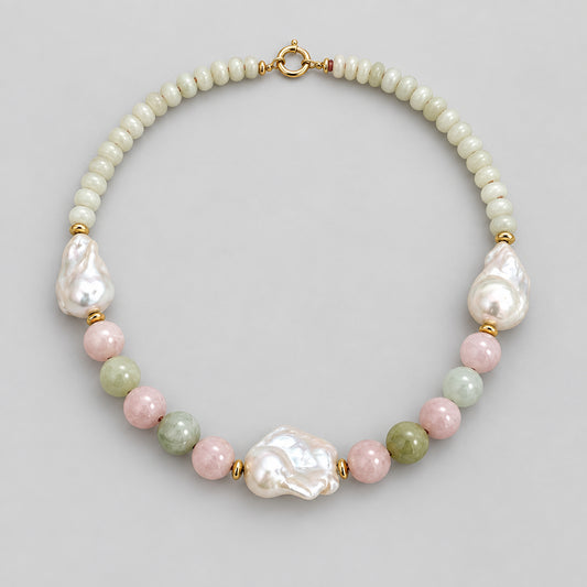 A handmade beaded necklace featuring a strand of small cream-colored beads, irregular white baroque pearls, polished pink and green beads, and gold spacer rings, displayed on a neutral light beige background.