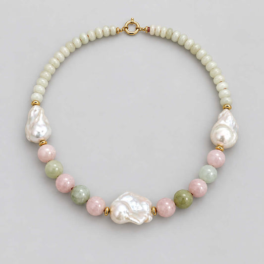 A handmade beaded necklace featuring a strand of small cream-colored beads, irregular white baroque pearls, polished pink and green beads, and gold spacer rings, displayed on a neutral light beige background.