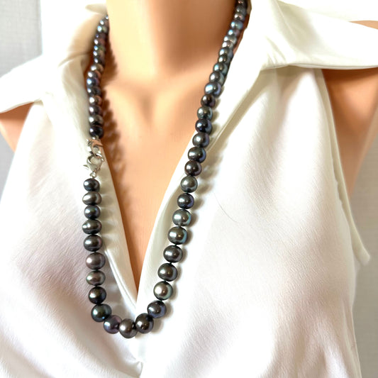 A dark gray pearl necklace with a silver-toned clasp, displayed on a mannequin torso wearing a white blouse.