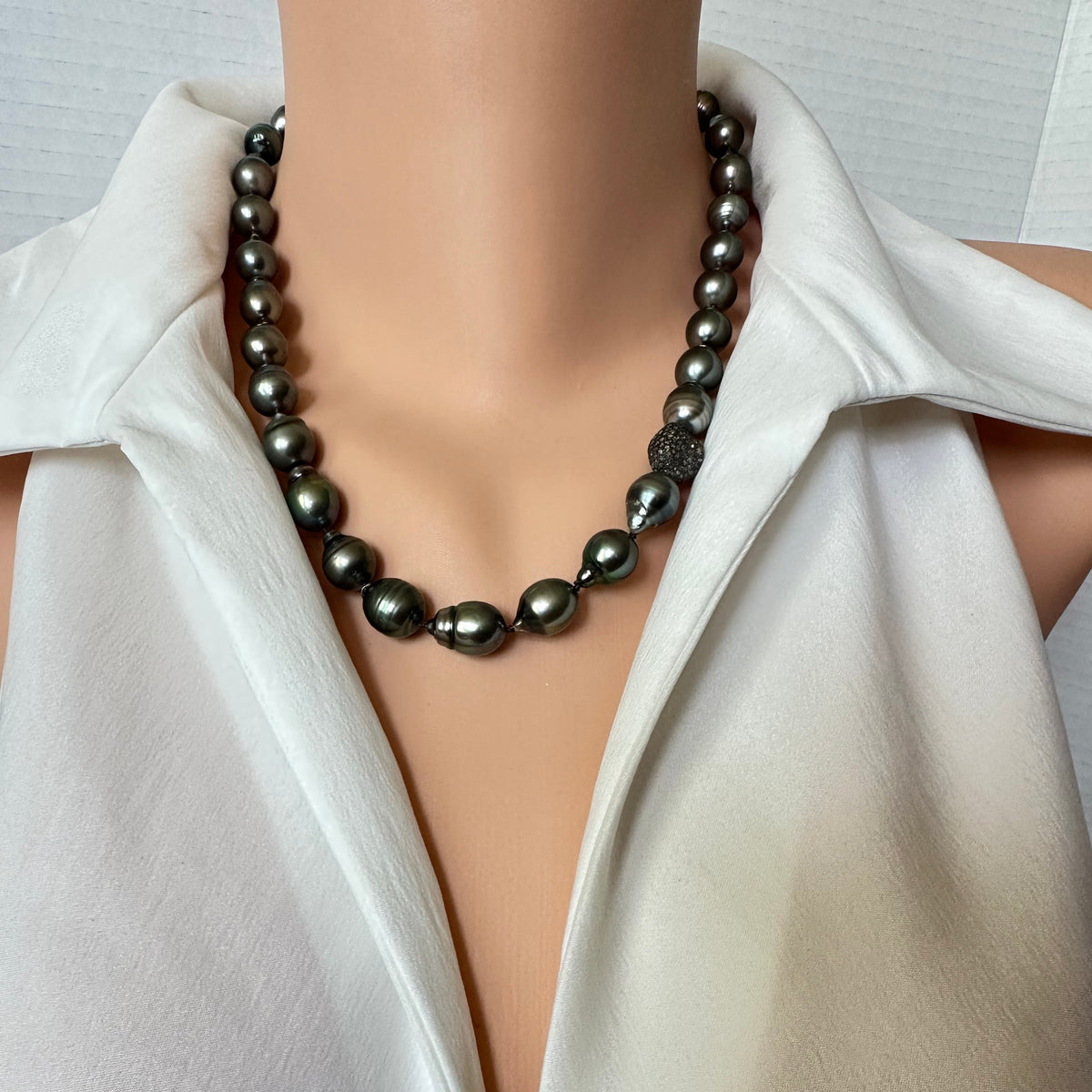 A dark gray baroque pearl necklace displayed on a mannequin torso wearing a white satin blouse.