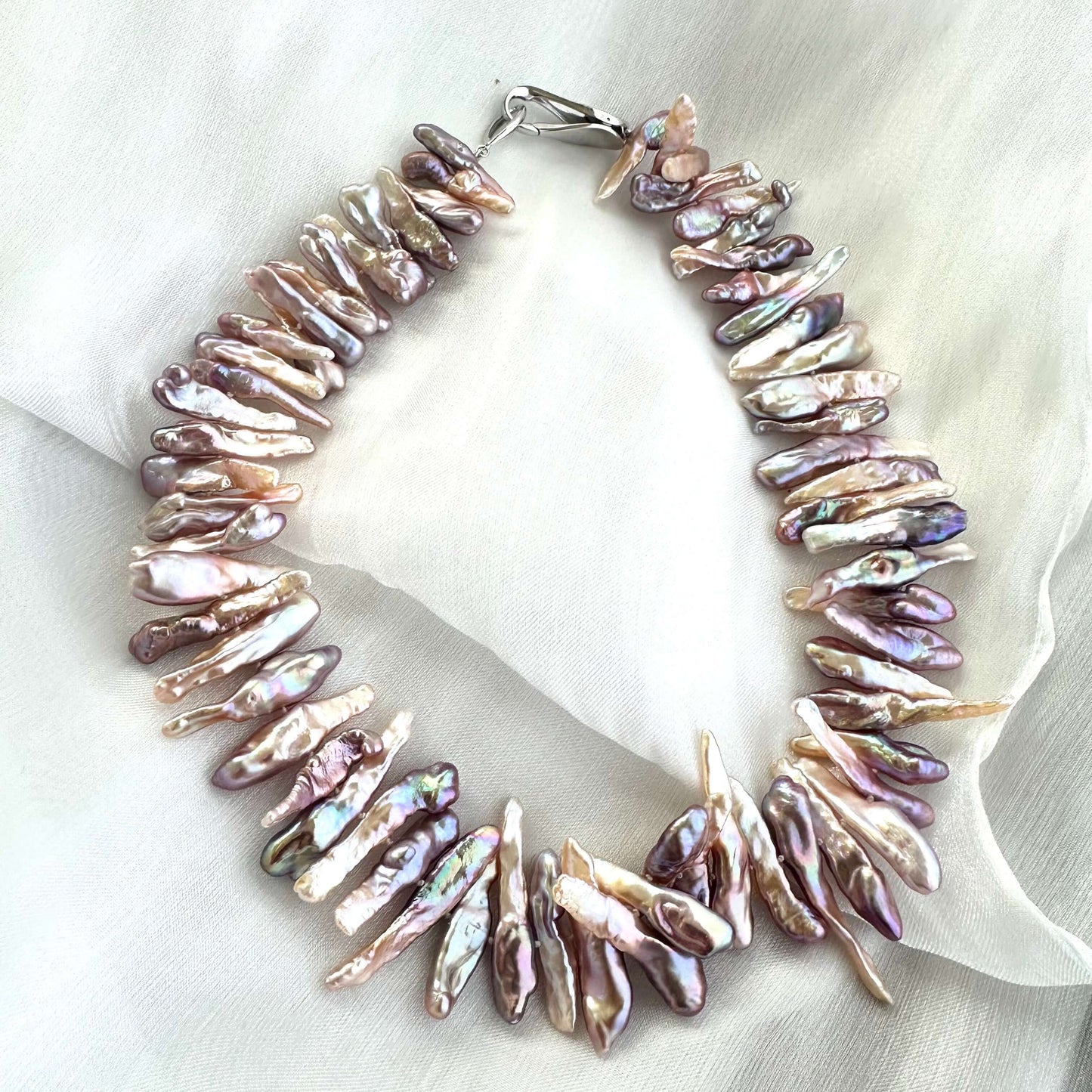Close-up of Biwa Pearl Necklace showing iridescent long stick pearls arranged on white cloth surface.
