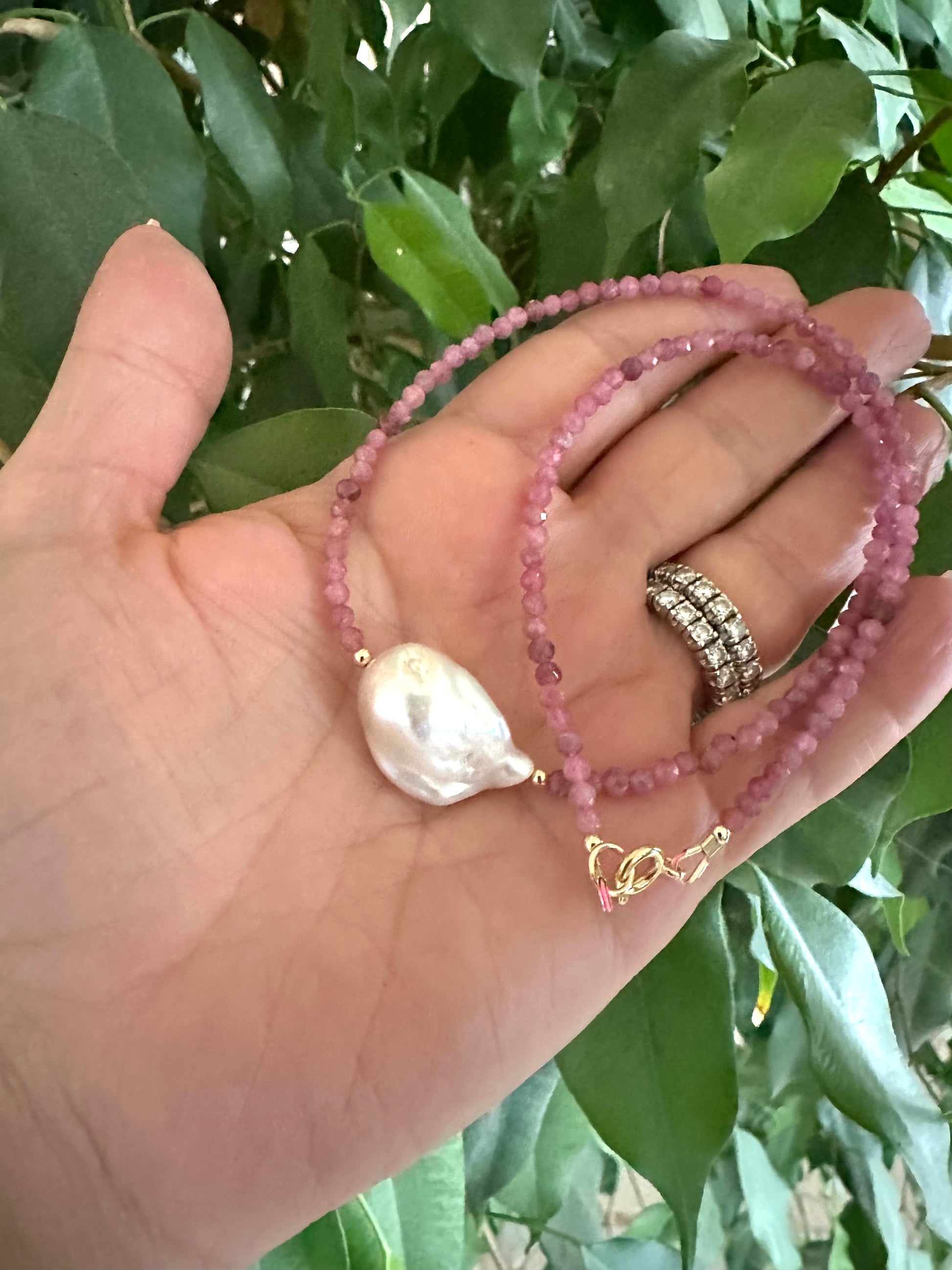 pink tourmaline baroque pearl necklace held in hand against green foliage