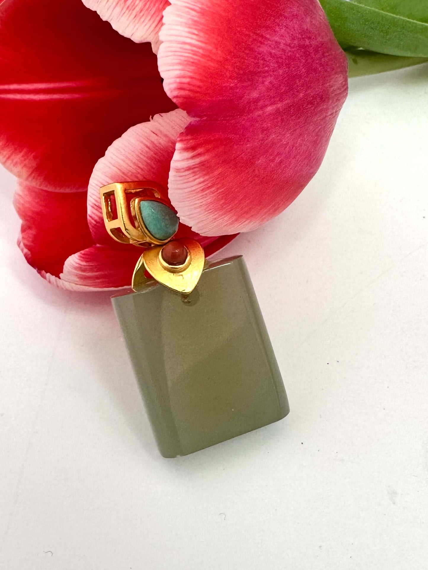 Hotan jade pendant with turquoise and red agate in gold vermeil resting beside a pink tulip flower.