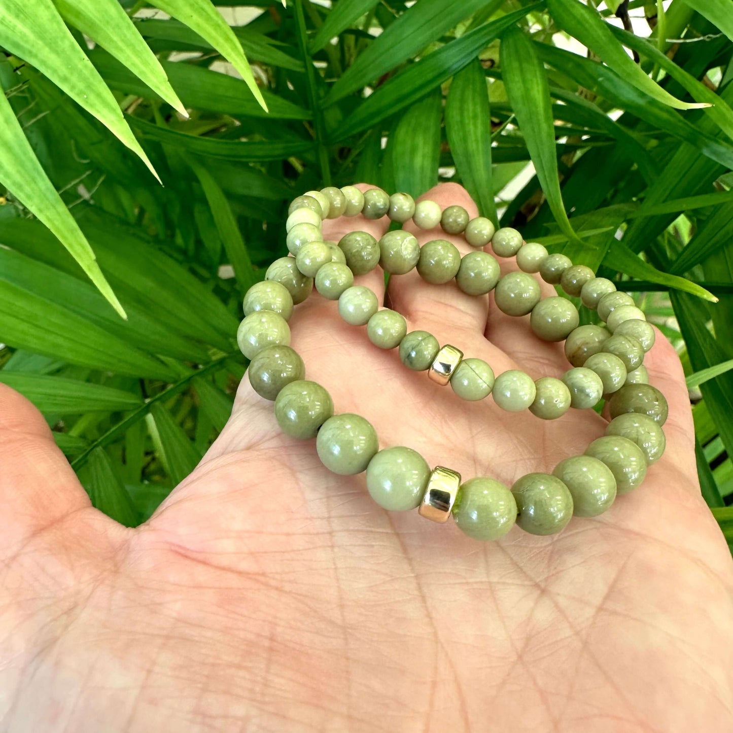 Olive green jasper bracelet showcasing 6mm and 8mm beads in a hand, featuring gold accents and lush green background.