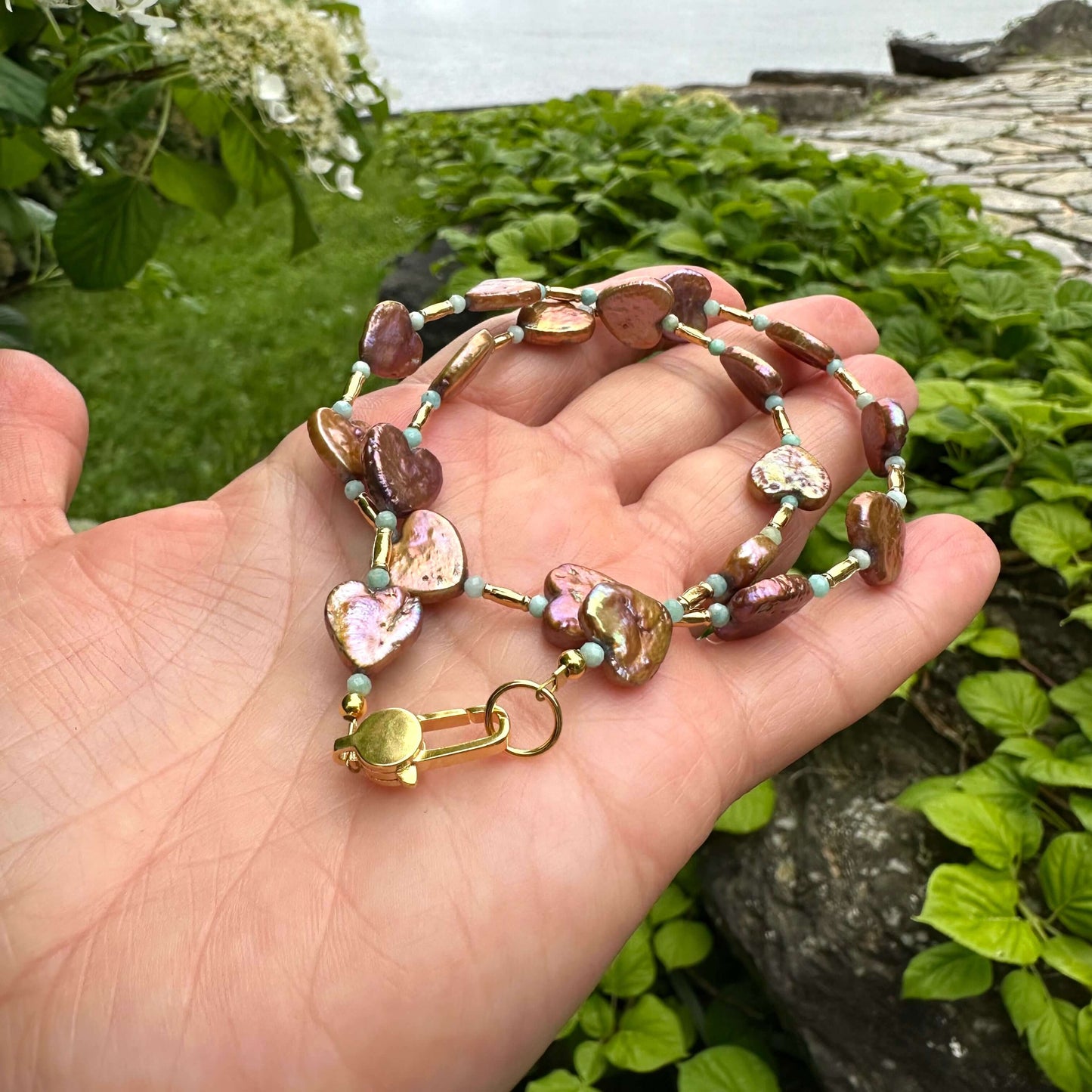 Bronze pearl choker with heart-shaped pearls held in hand against green foliage