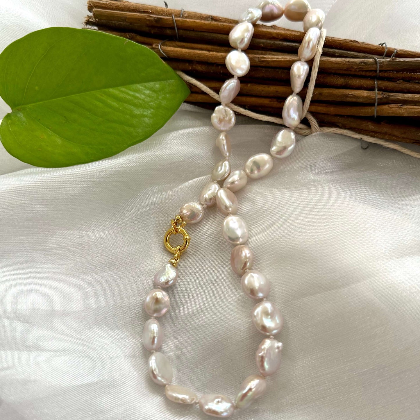 Coin pearl necklace with gold marine clasp displayed on white cloth