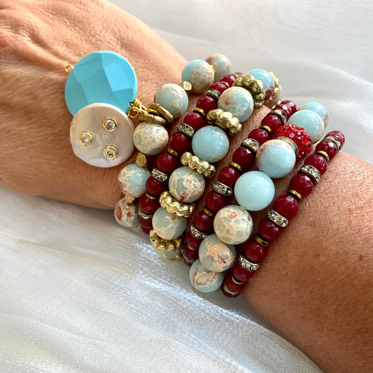 Pale blue deep red stretchy bracelet stack worn on wrist showing mixed gemstones and charms