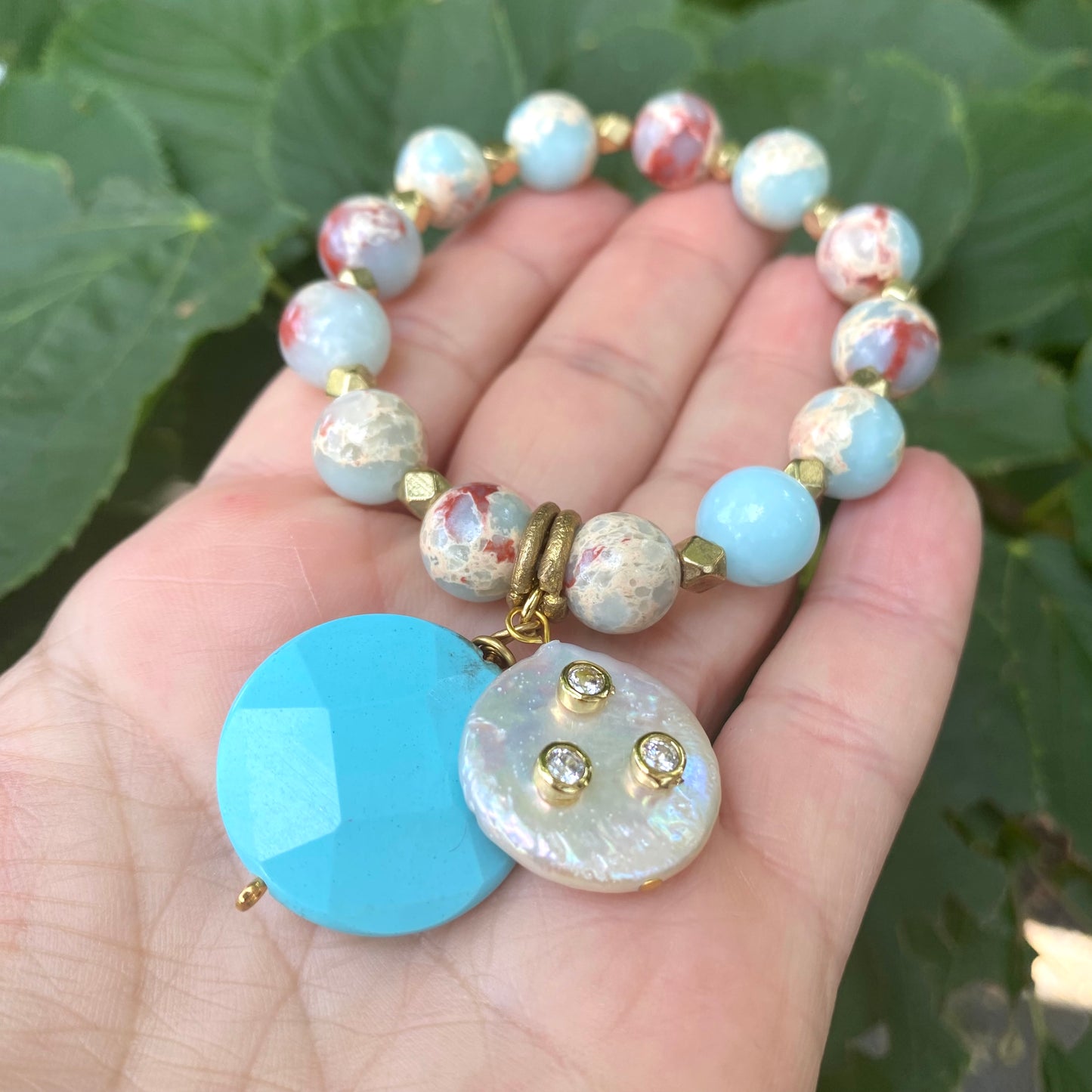 Pale blue deep red stretchy bracelet close-up highlighting charms, pearls, and blue tones