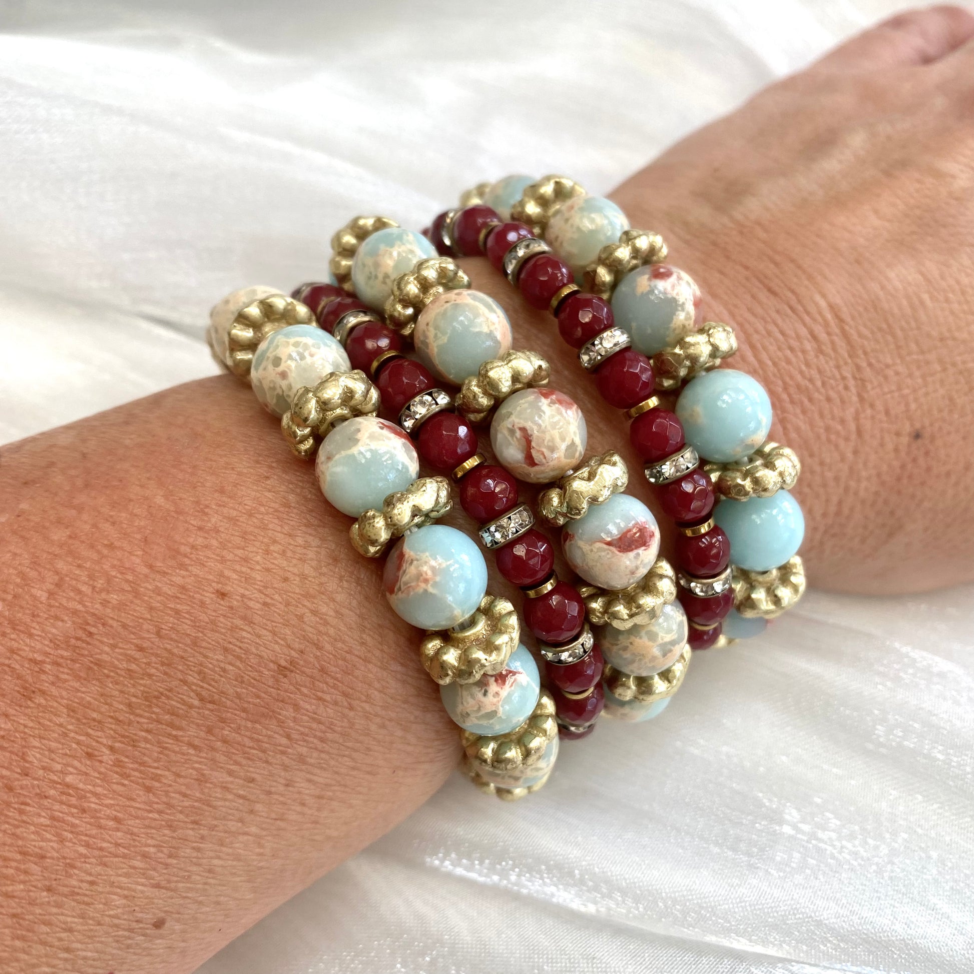 Pale blue deep red stretchy bracelet stack styled on wrist with brass and pearl accents