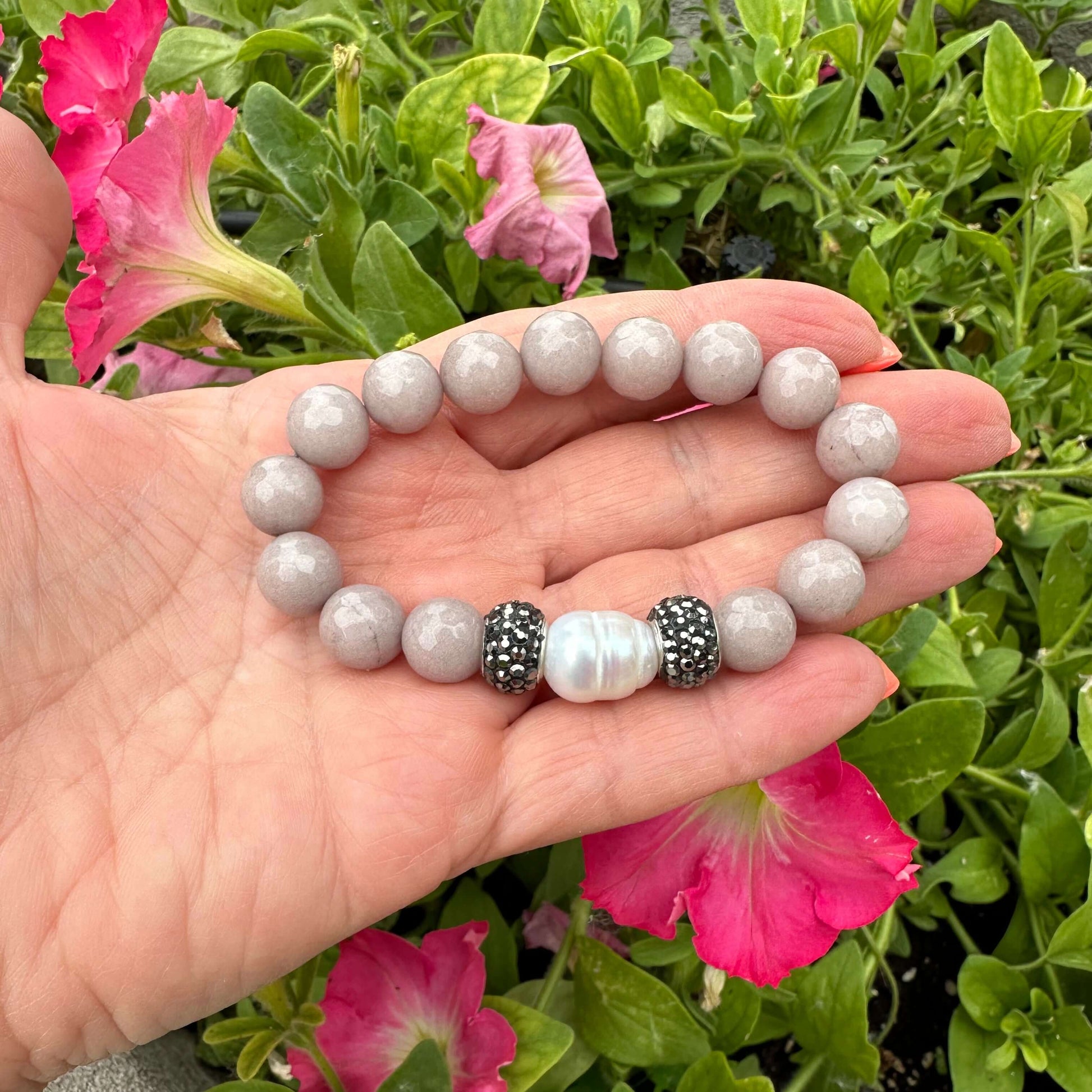 Pink jade pearl bracelet held in hand against green foliage