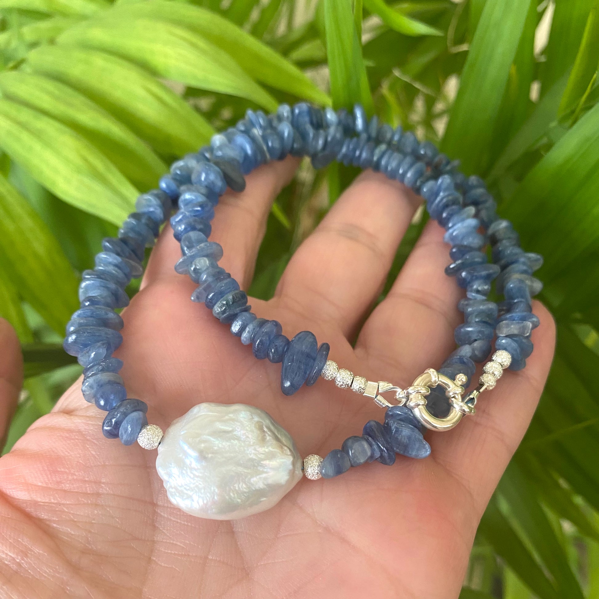 Blue kyanite pearl necklace held in hand against green leaves