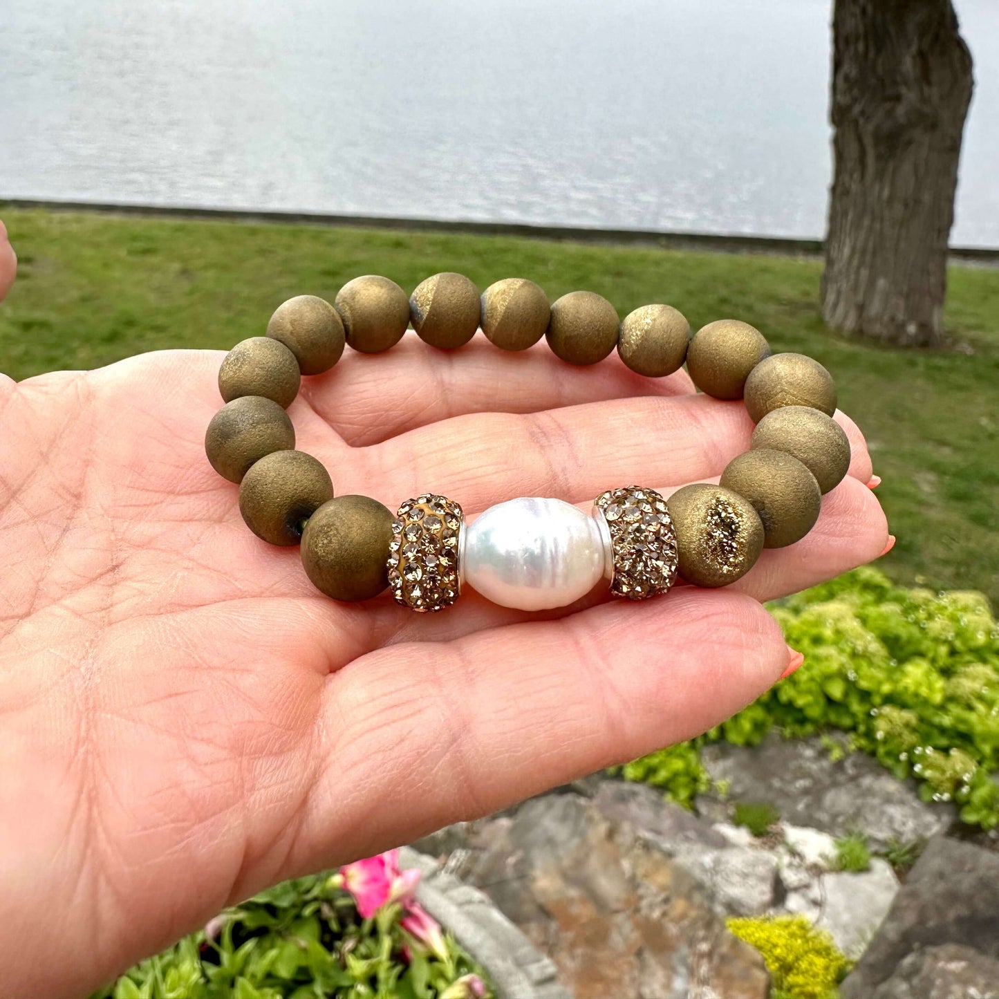 Gold druzy agate bracelet held in hand against green summer foliage