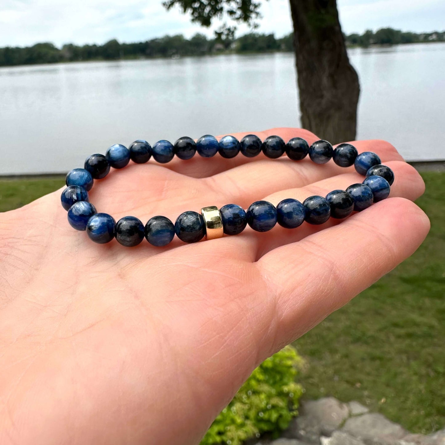 Blue kyanite bracelet held in hand against green outdoor foliage