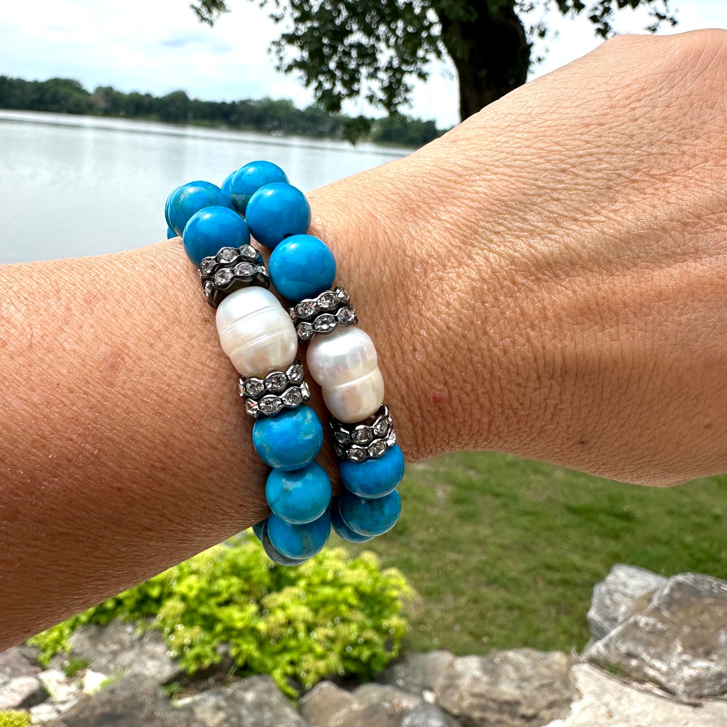 Turquoise howlite pearl bracelets worn on wrist beside garden lake