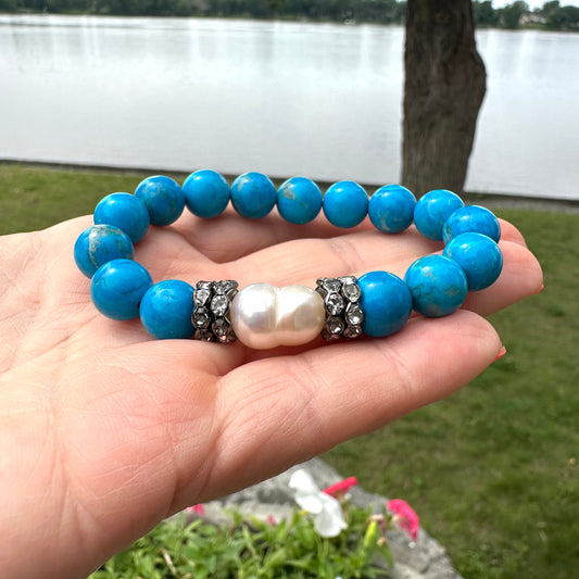 Turquoise howlite pearl bracelet held in hand against natural foliage