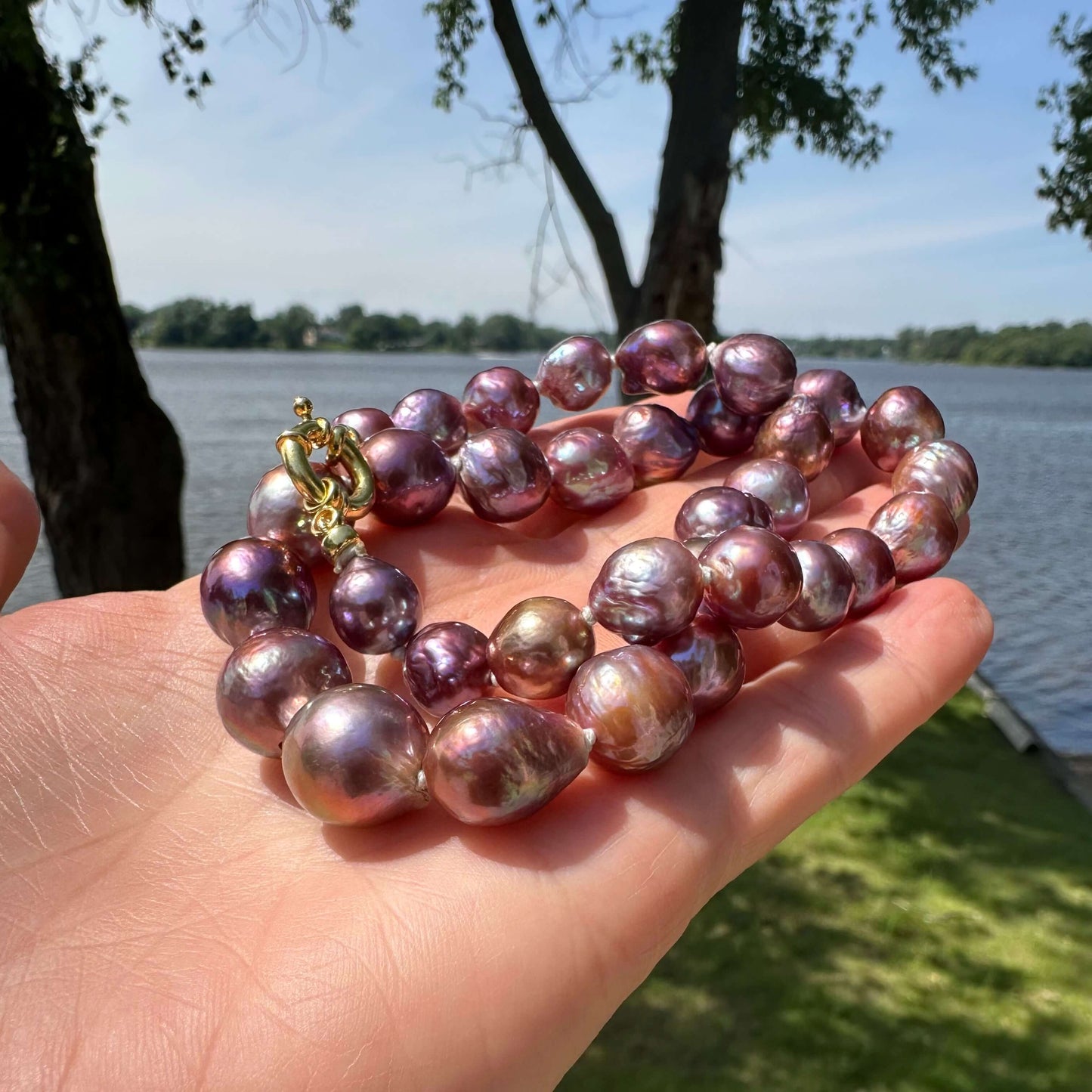 Close-up of purple Edison baroque pearl necklace held outdoors near greenery