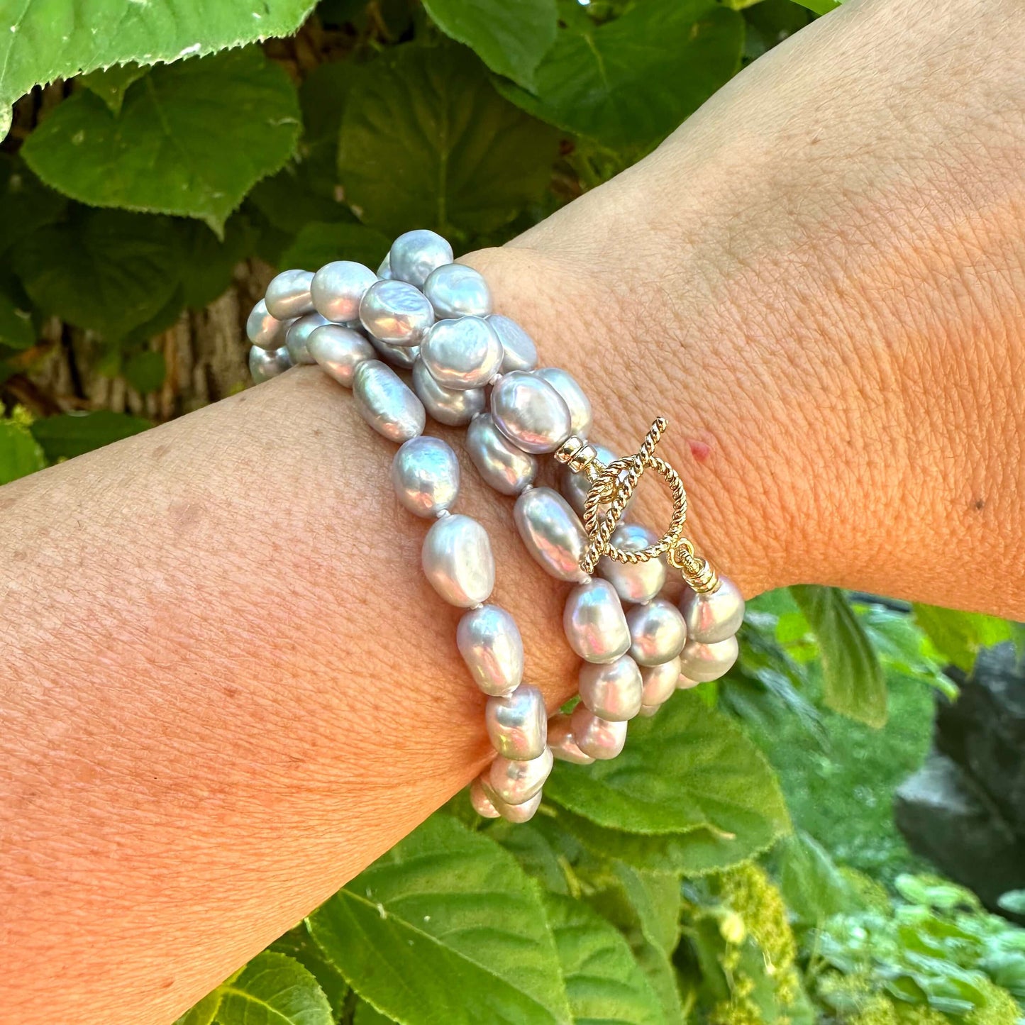 Close-up of grey nugget pearl necklace wrapped around wrist outdoors near foliage