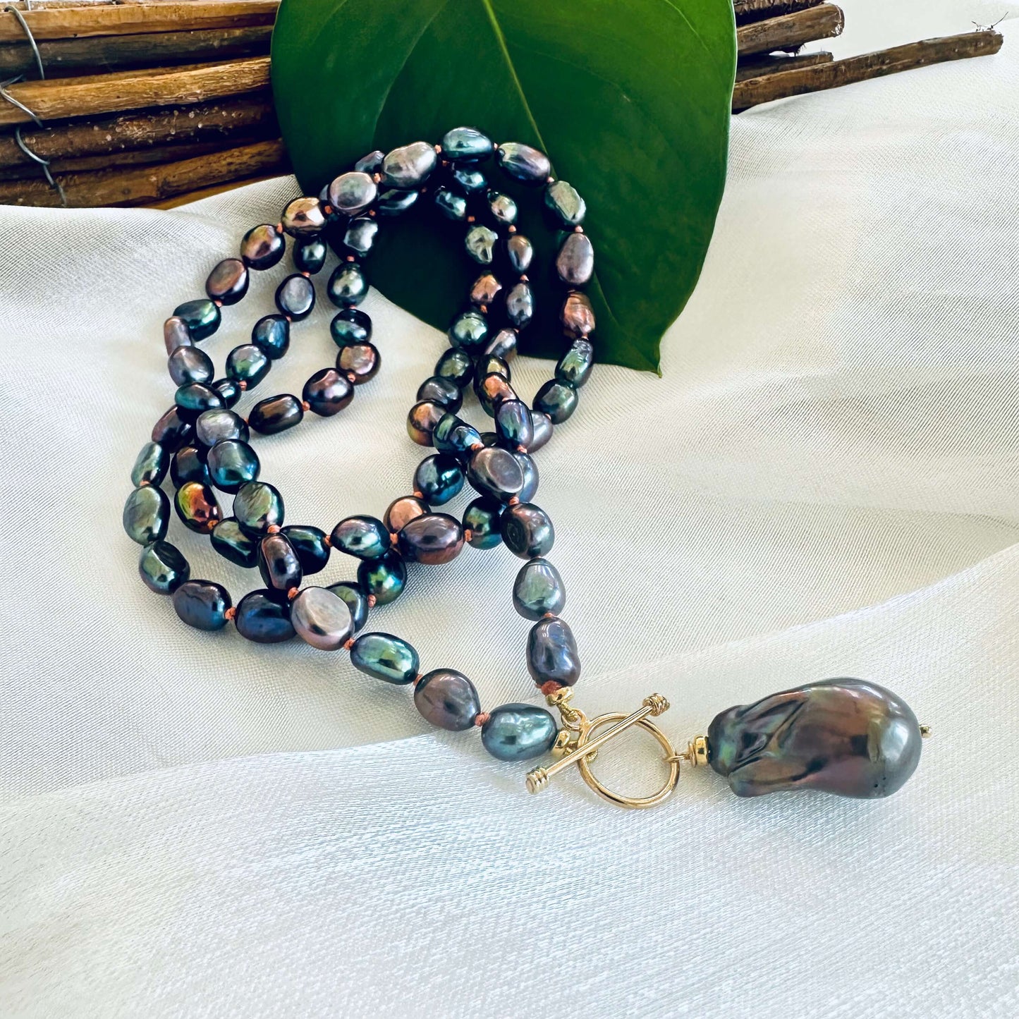 Peacock black pearl necklace with baroque pendant displayed on white cloth