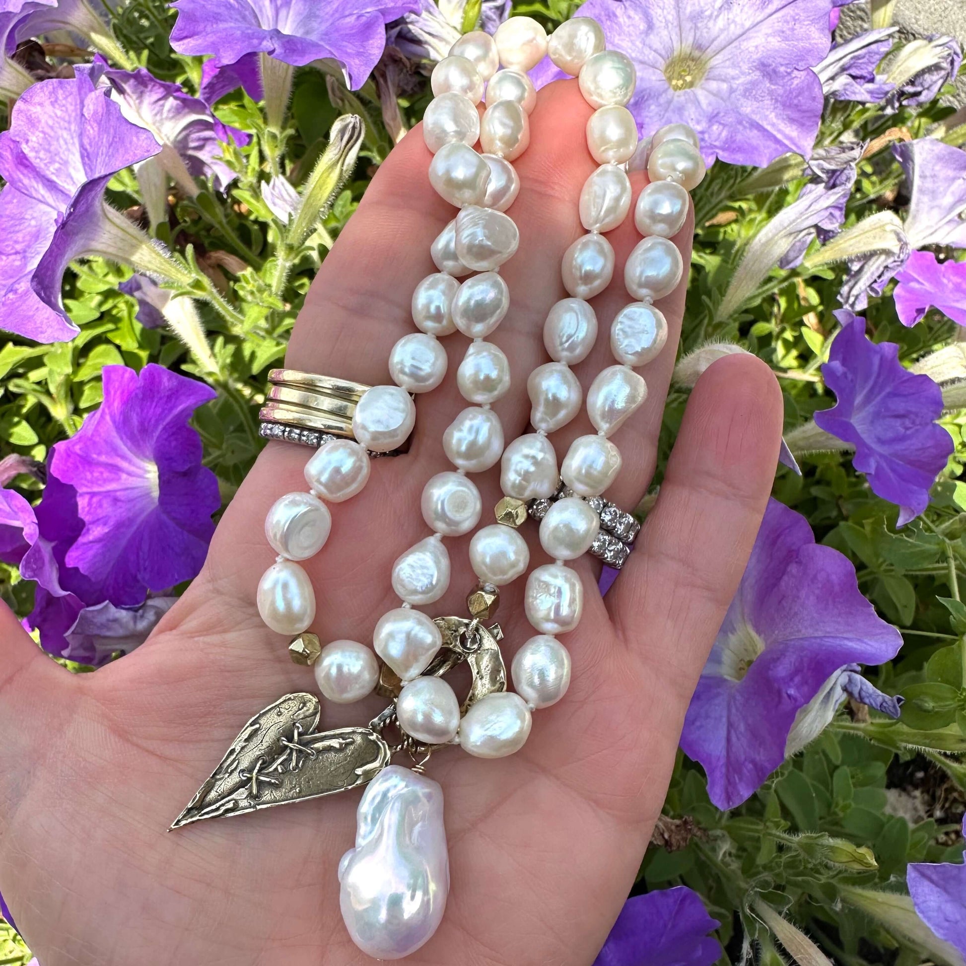 Pearl toggle necklace with heart and baroque pearl pendants held in hand near foliage