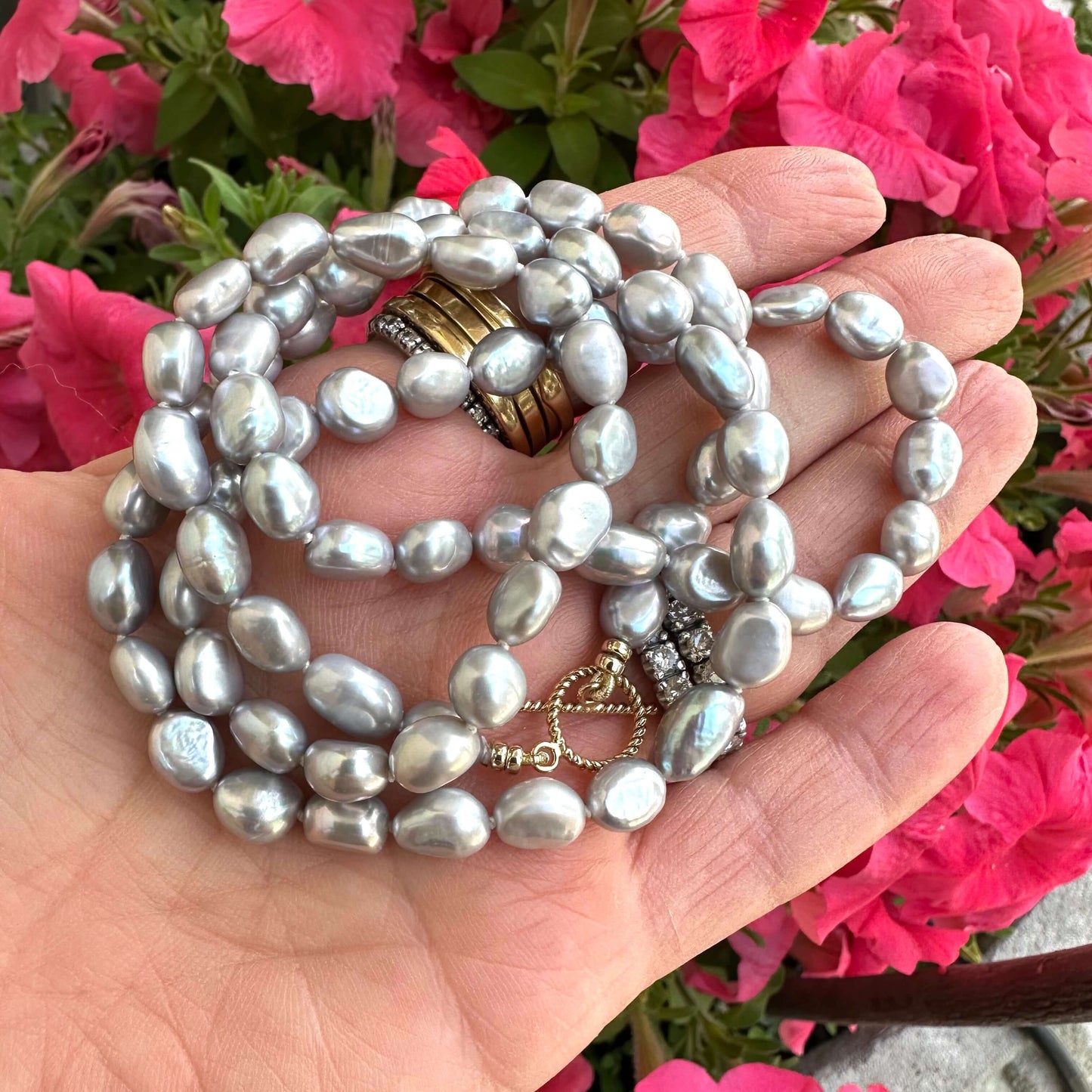 Grey nugget pearl necklace held in hand against pink flowers