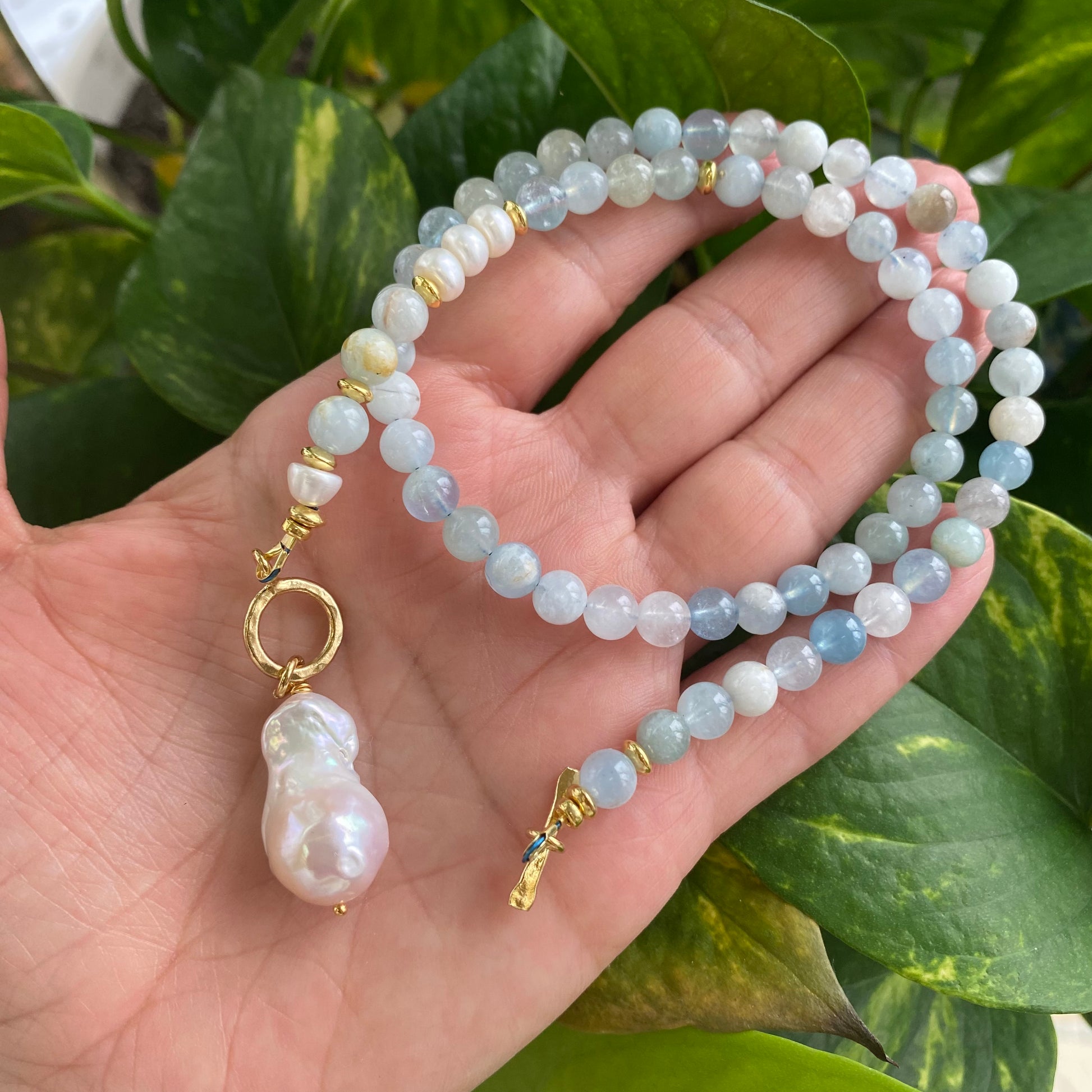 Aquamarine pearl necklace held in hand against green leaves