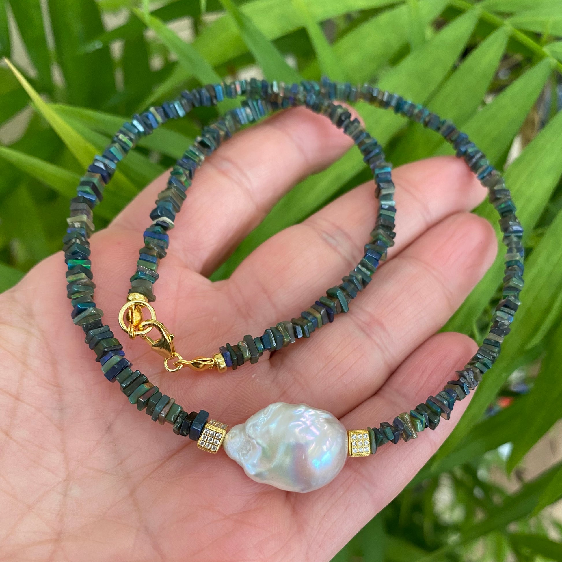 Black opal pearl necklace in hand with natural stone colors visible