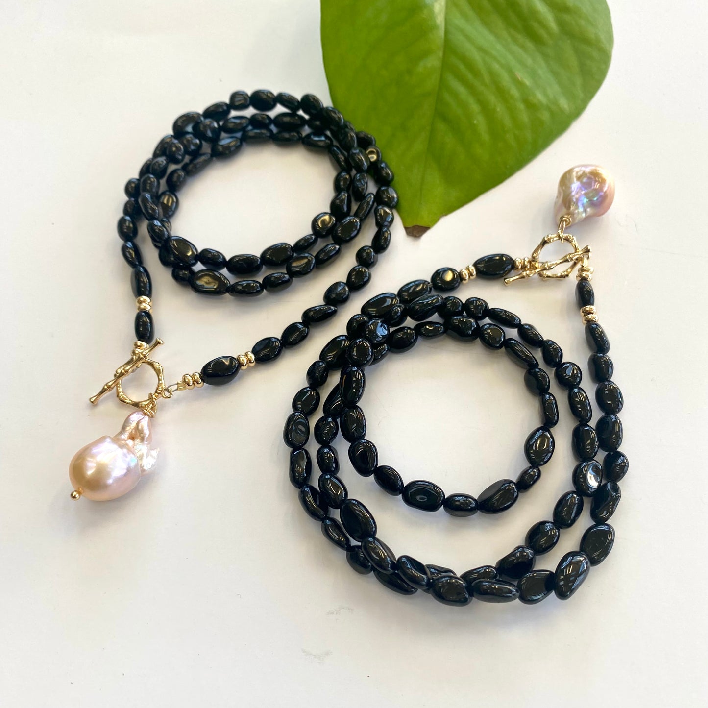 Black tourmaline pearl necklace displayed on white cloth table, size comparison