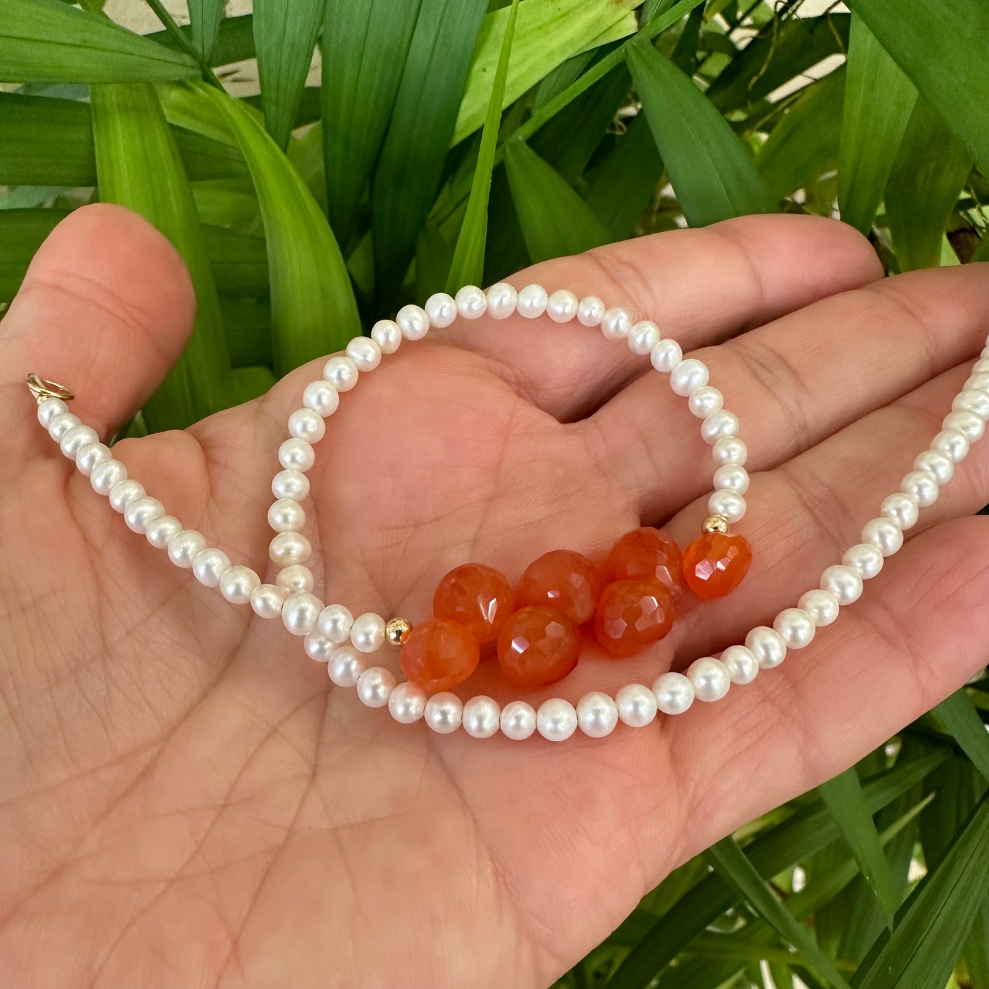 Double strand pearl bracelet held in hand against green foliage, showing natural light reflection