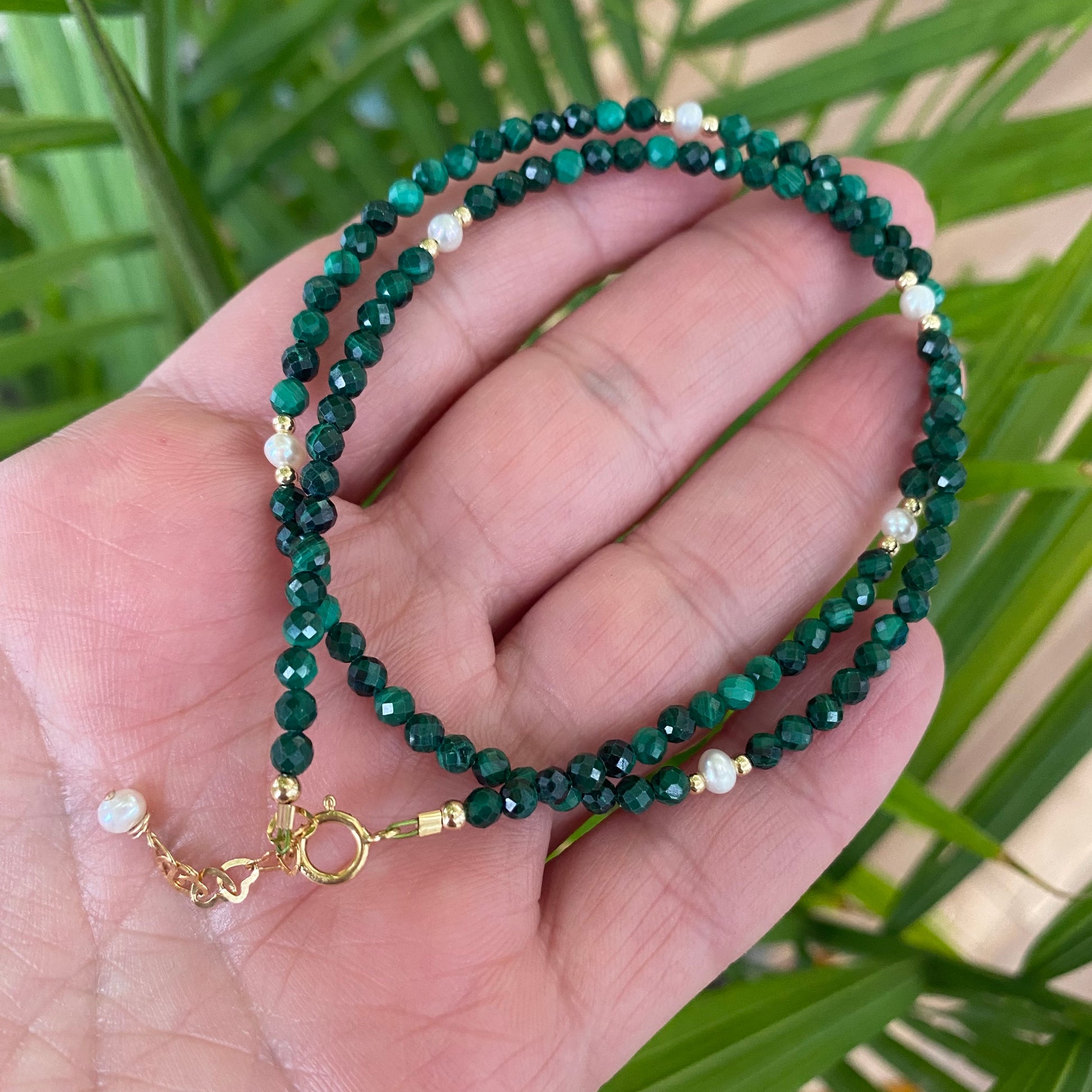 Malachite pearl choker necklace held in hand against green foliage