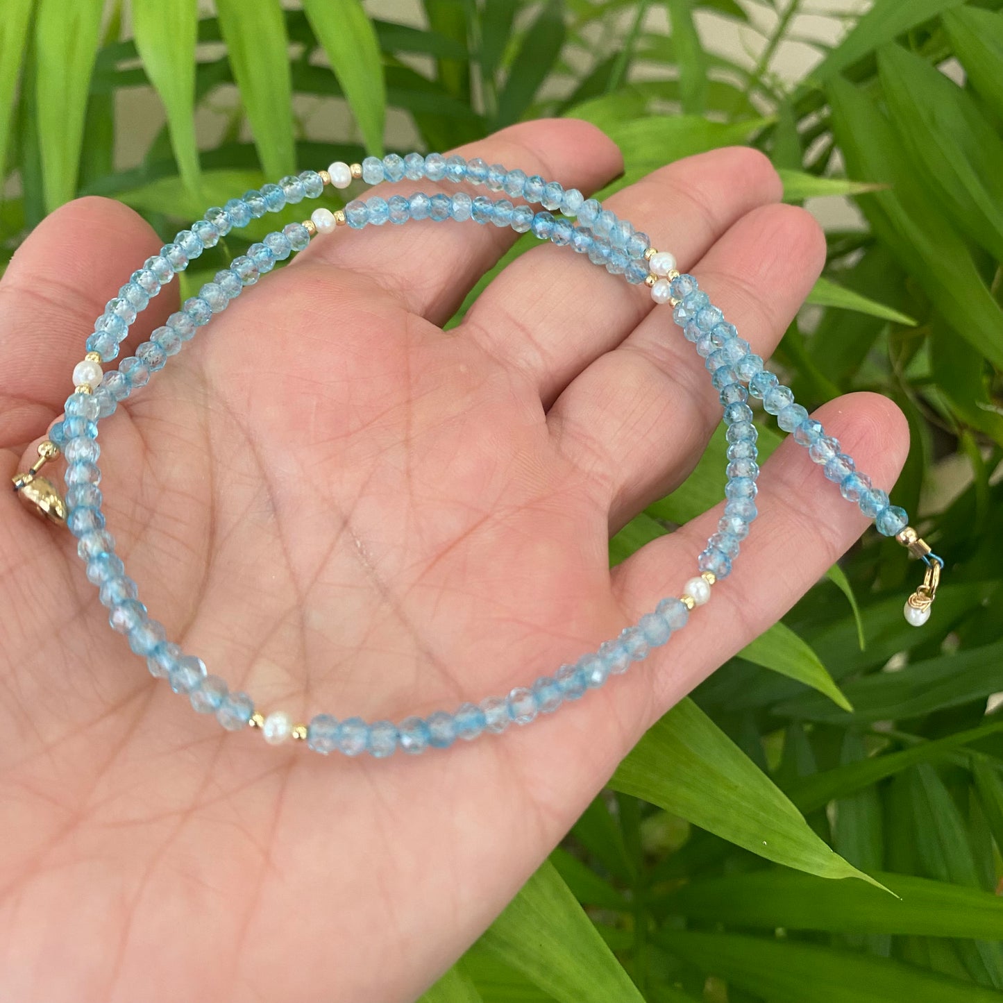 Blue topaz pearl choker necklace in hand with natural foliage background