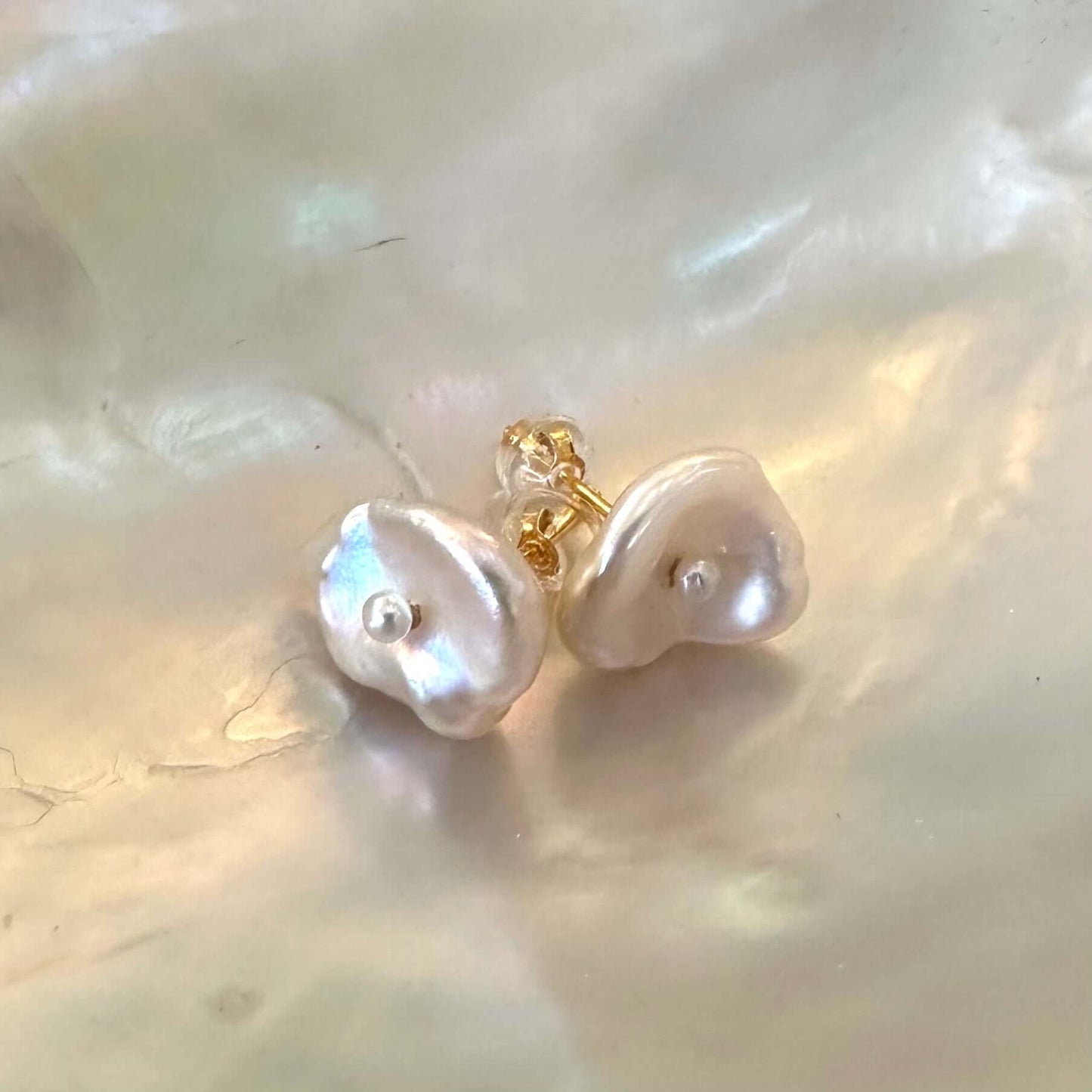 White flower pearl stud earrings displayed on white pearl shell, showing petal-shaped Keshi pearls with small central accents.