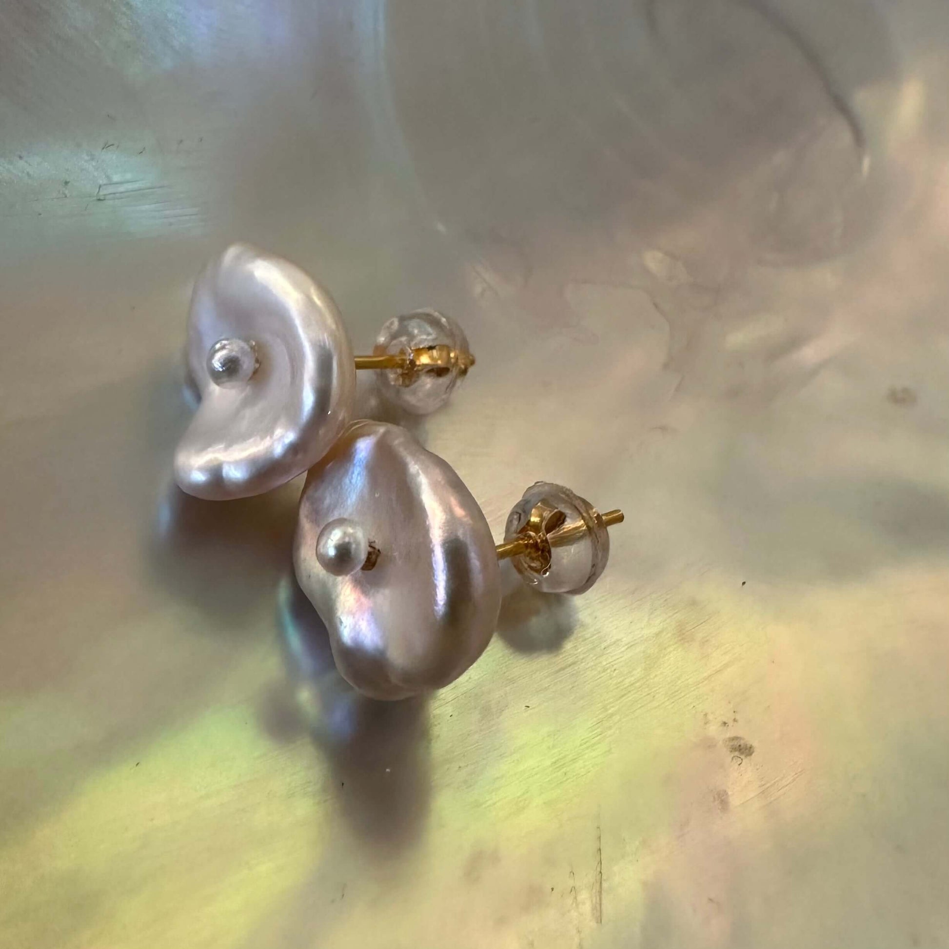 White flower pearl stud earrings resting on shell, highlighting handcrafted petal texture and luminous Keshi pearl luster.