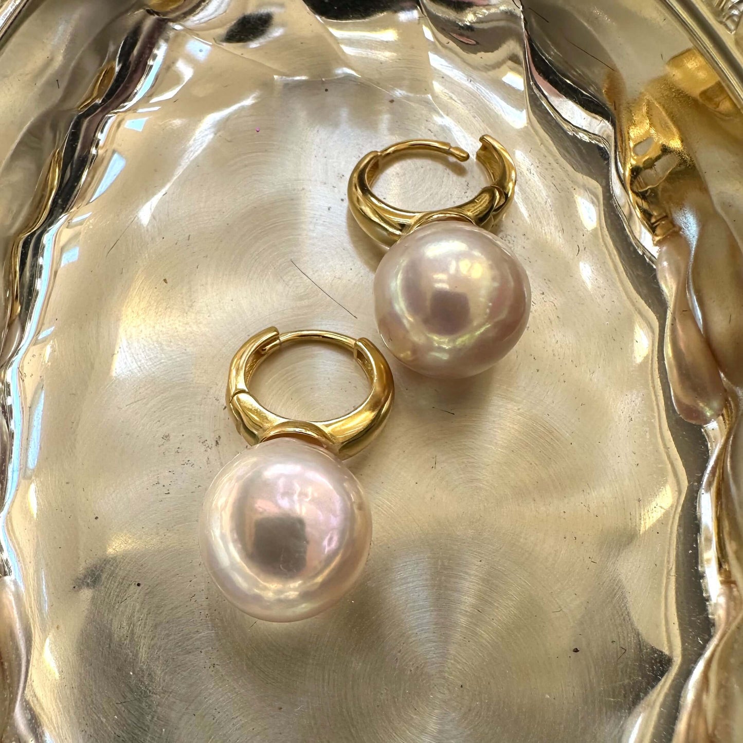 Golden pink pearl hoop earrings with Edison pearls on white shell, showing mirror-like shine and smooth round surfaces.