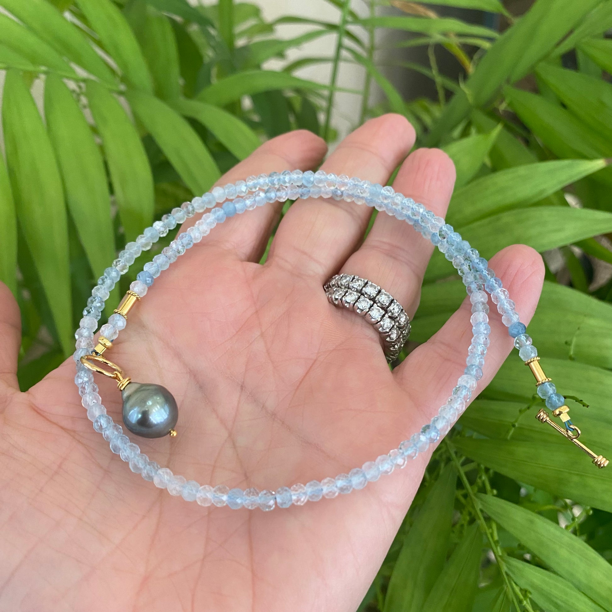 Aquamarine Pearl Pendant Necklace with Tahitian Baroque Pearl on a hand, surrounded by green foliage.