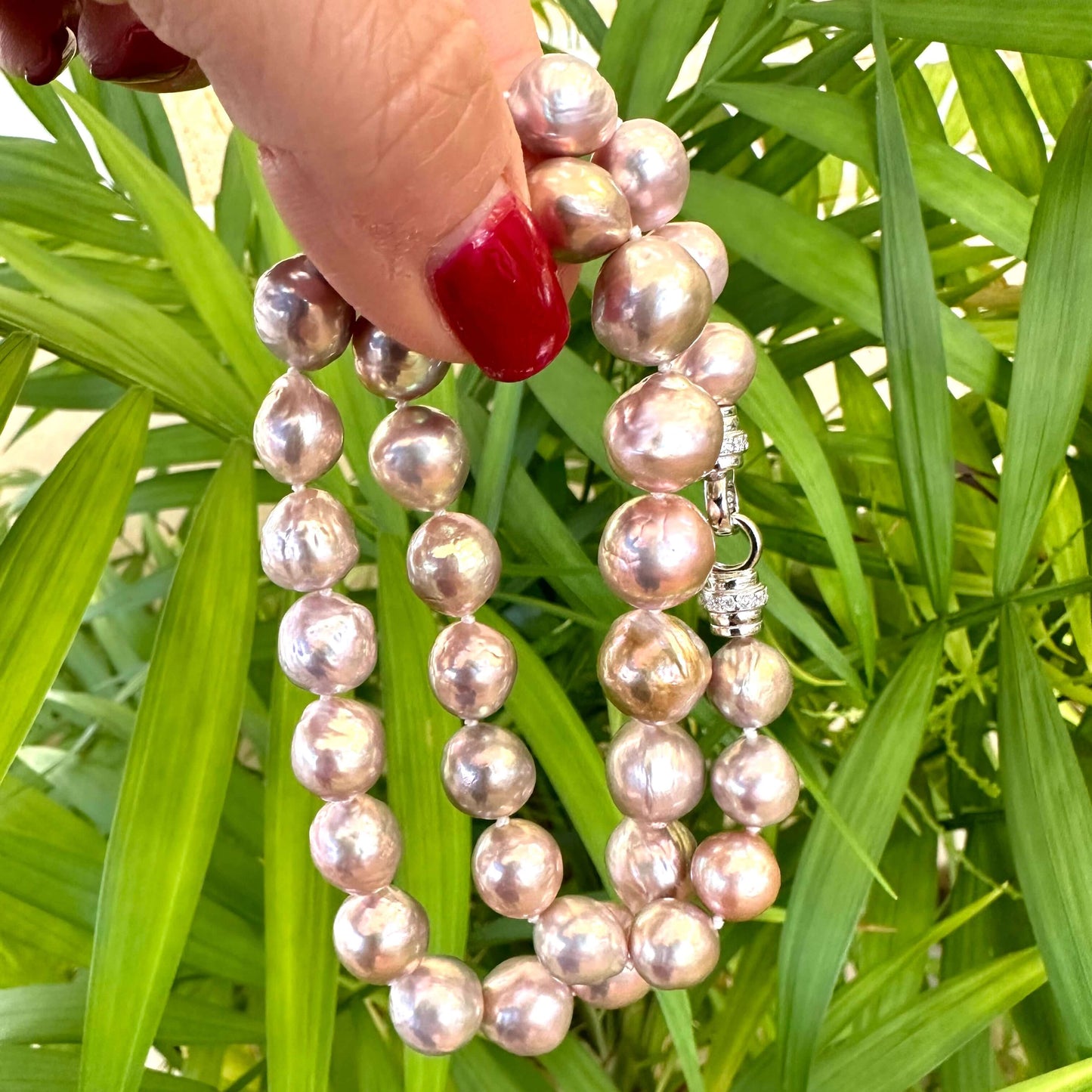 Hand holding pink lavender pearl necklace outdoors, highlighting soft iridescent tones and authentic baroque pearls.