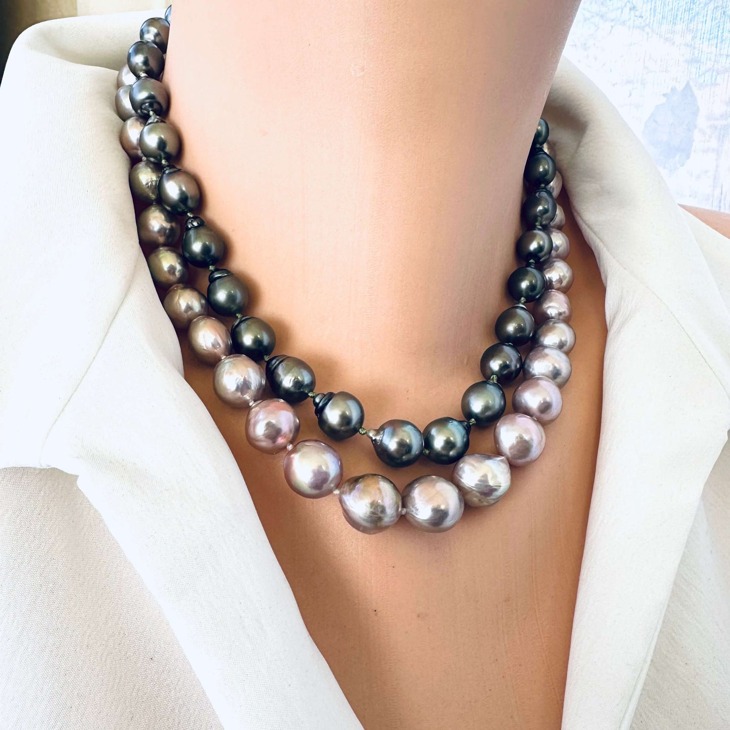 Pink lavender pearl necklace displayed beside darker Tahitian pearl strand on mannequin, showing color contrast and size.