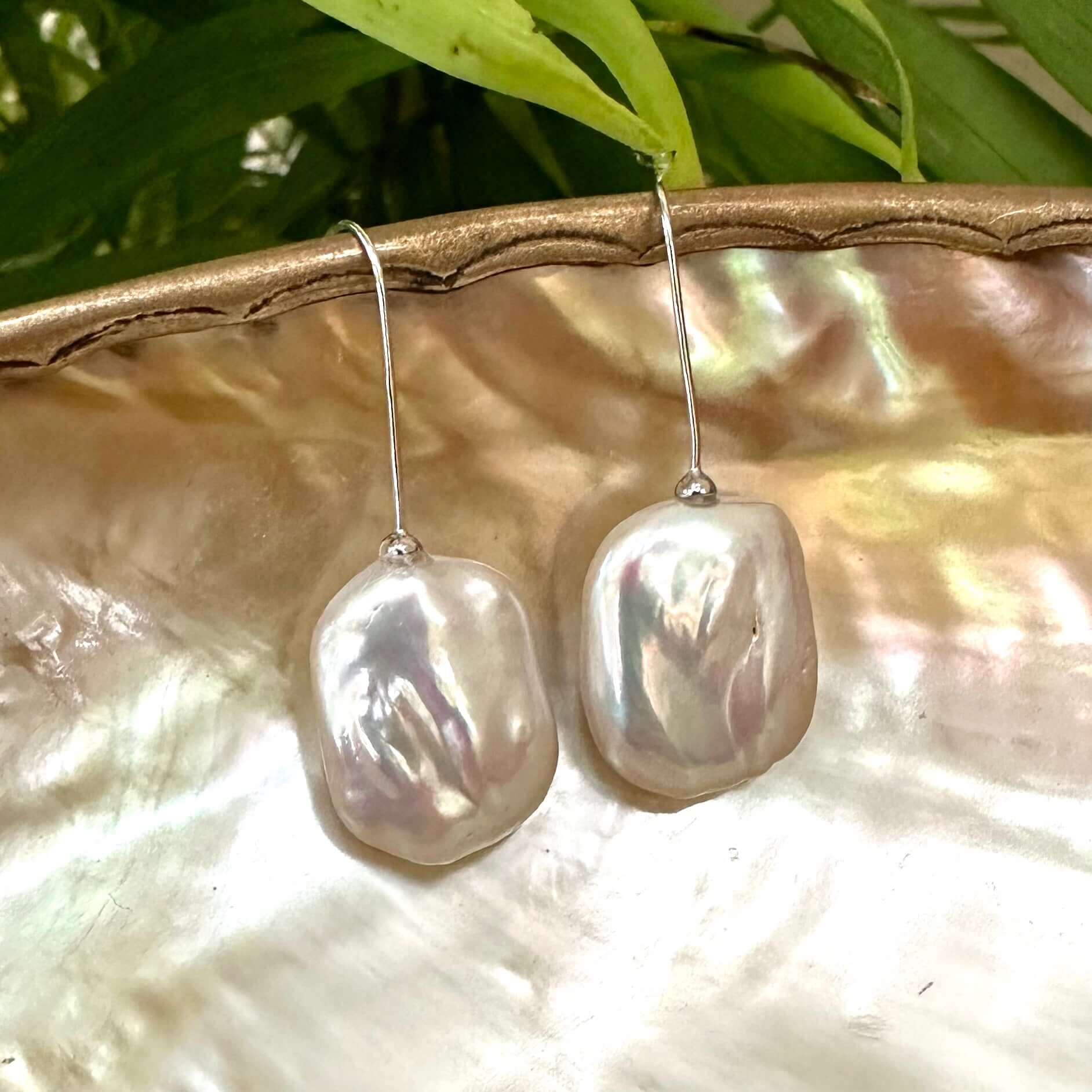 White freshwater pearl drop earrings rhodium-plated silver displayed on pearl shell with green leaf background, designed and handmade in Canada.