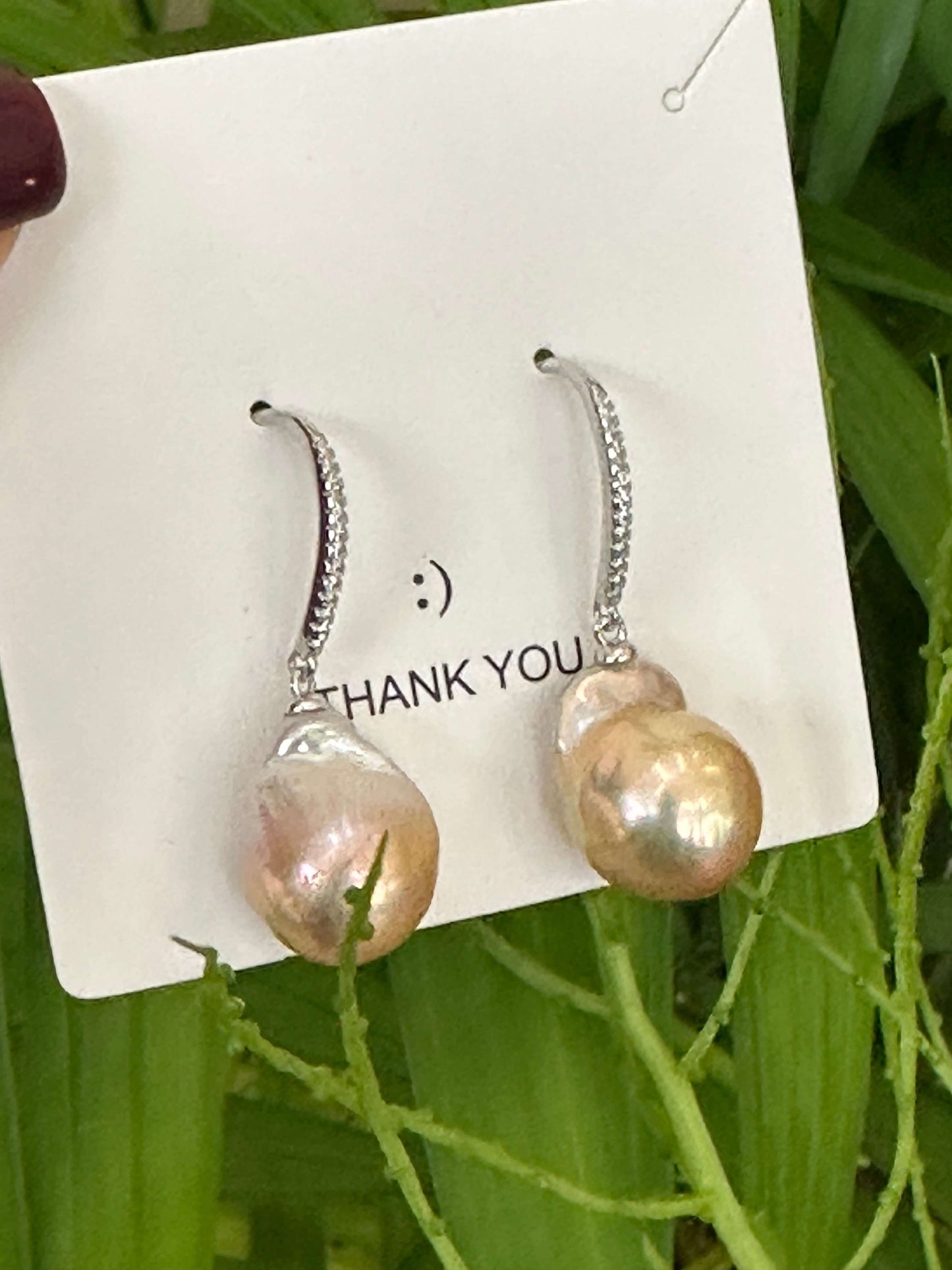 Golden pink baroque pearl dangle earrings with CZ pavé silver hooks held near green leaves, handcrafted in Canada.