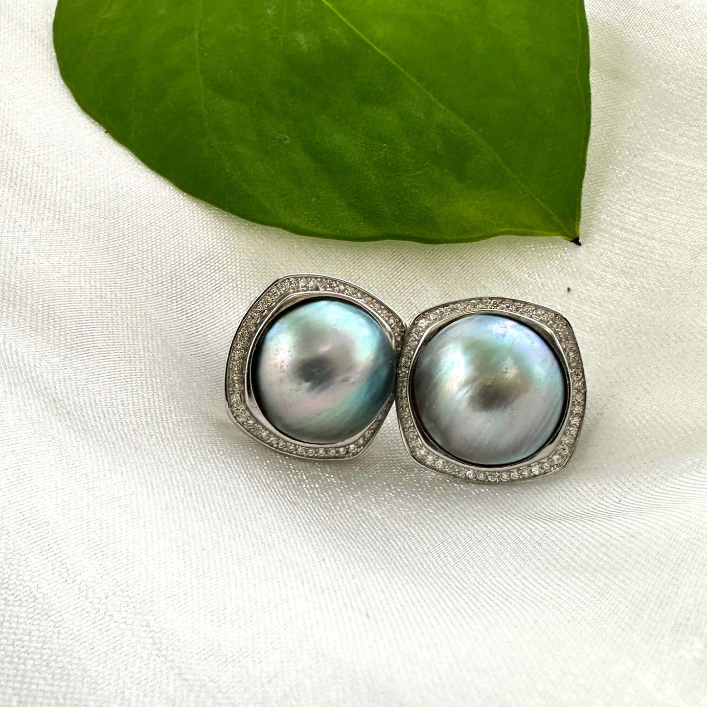 Mabe Pearl Earrings – shown on white cloth with green leaf accent