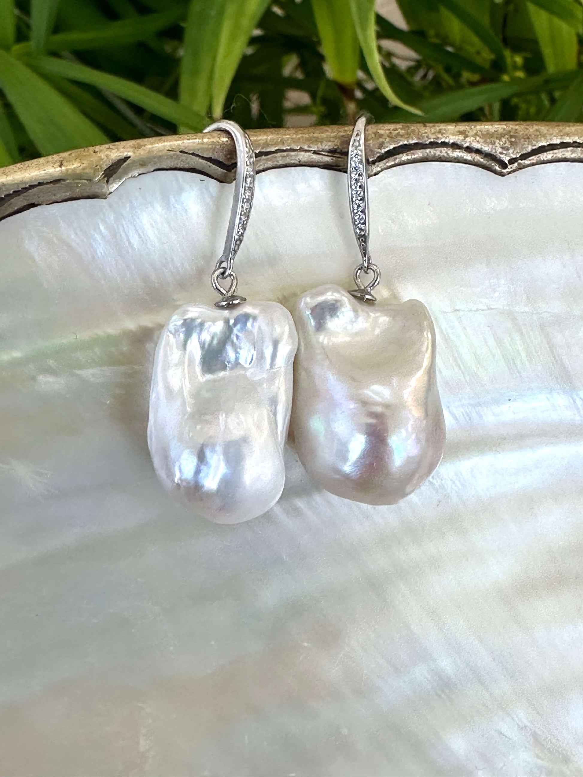 White baroque pearl bridal earrings detailed view on pearl shell beside green leaves, elegant handcrafted jewelry from Canada.