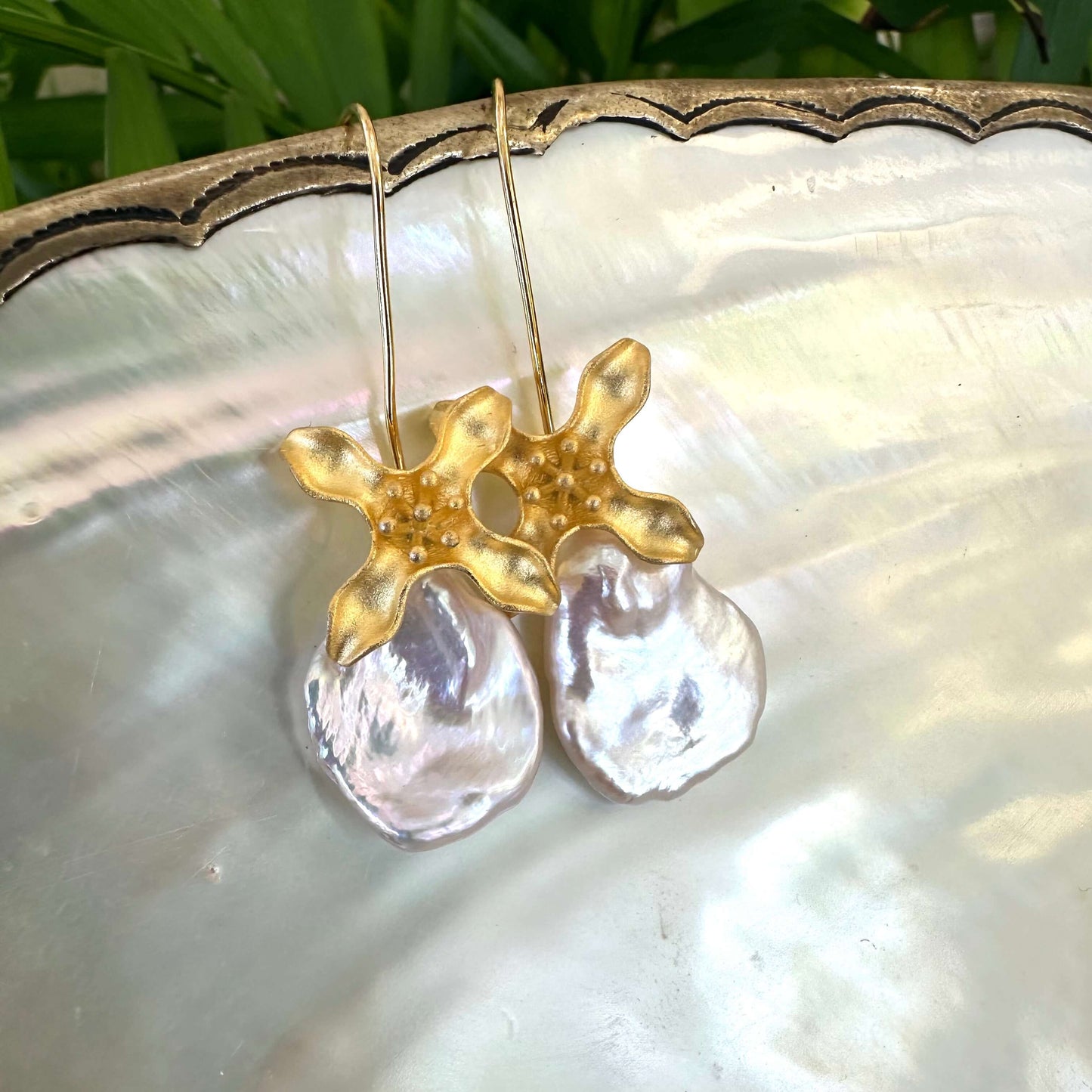 Detailed close-up of white Keshi Pearl Earrings with flower hooks on pearl shell surface.