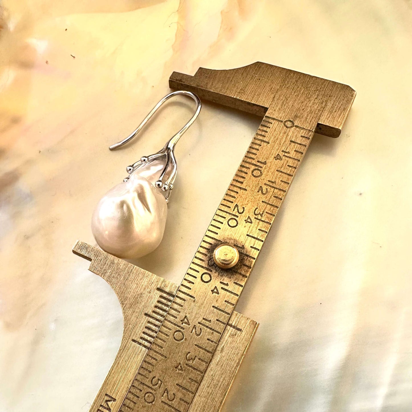 Close-up of white baroque pearl drop earrings measured against ruler on white pearl backdrop – handmade in Canada